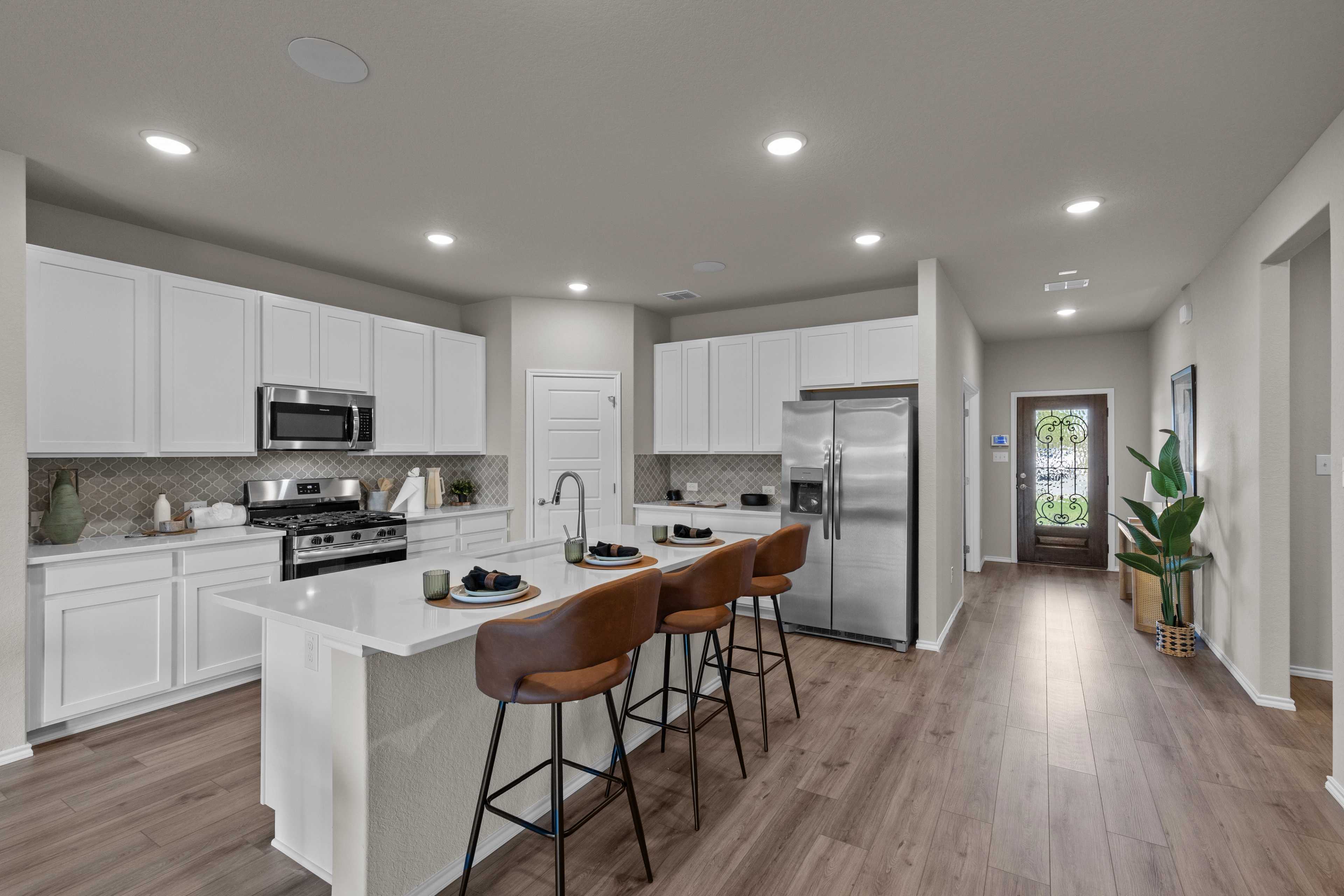 Spacious modern kitchen in Comanche Ridge San Antonio TX with white cabinets, stainless steel appliances, island bar stools, hardwood floors