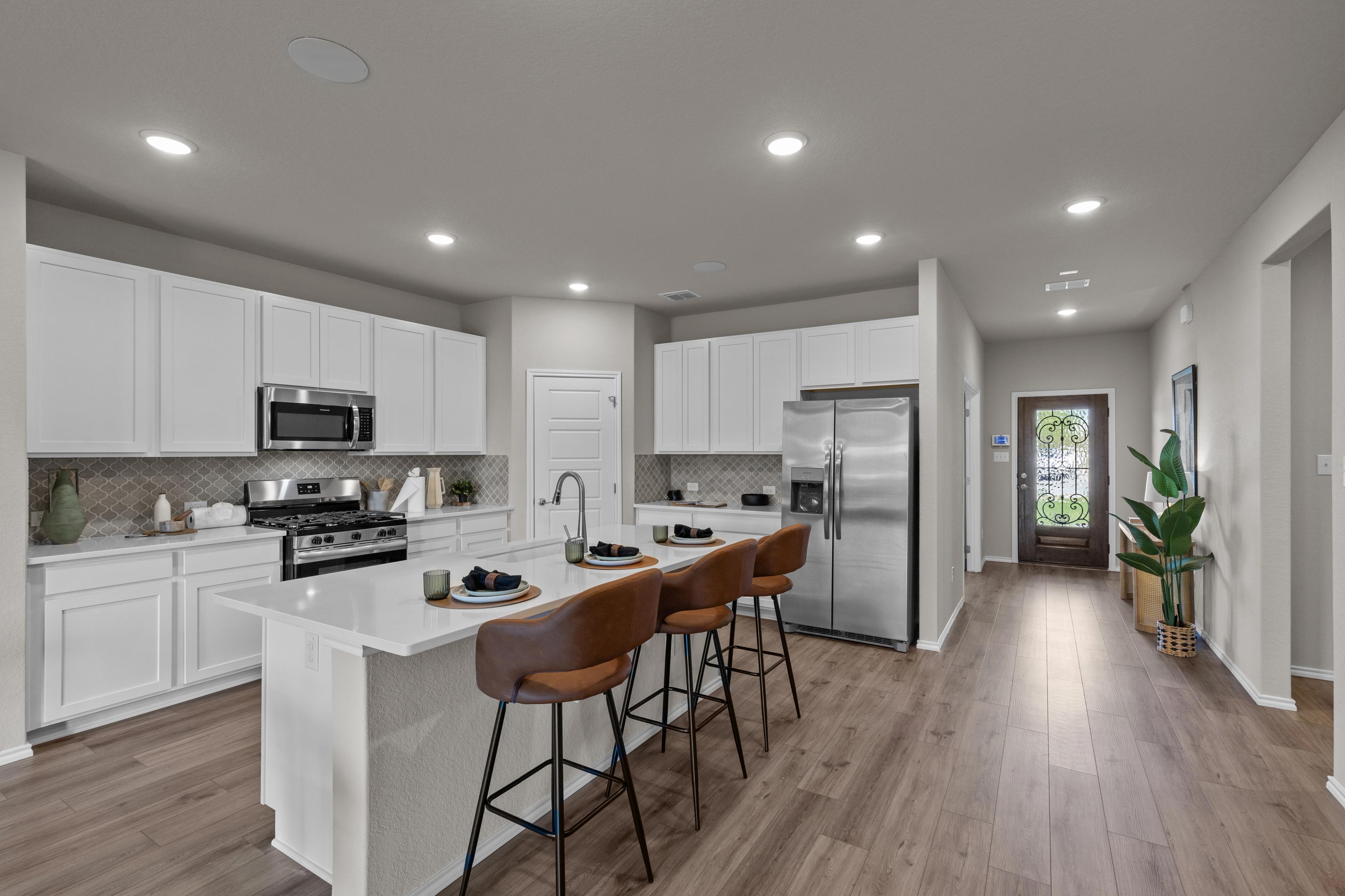 Spacious modern kitchen in Comanche Ridge San Antonio TX with white cabinets, stainless steel appliances, island bar stools, hardwood floors