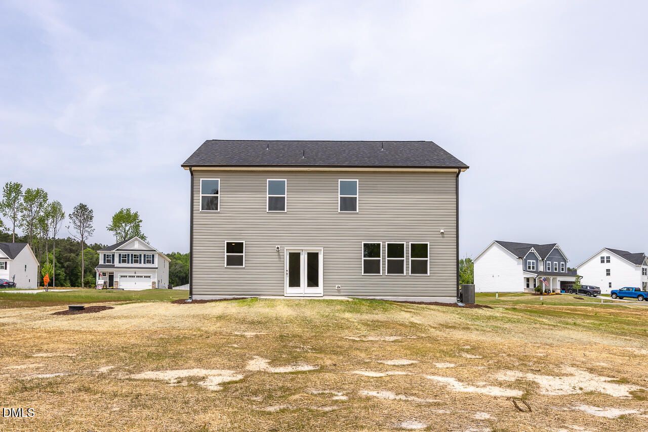 Rear view of two-story gray 5-bedroom home with large windows, double doors, and grassy backyard in Woodland Crossing, Zebulon, NC
