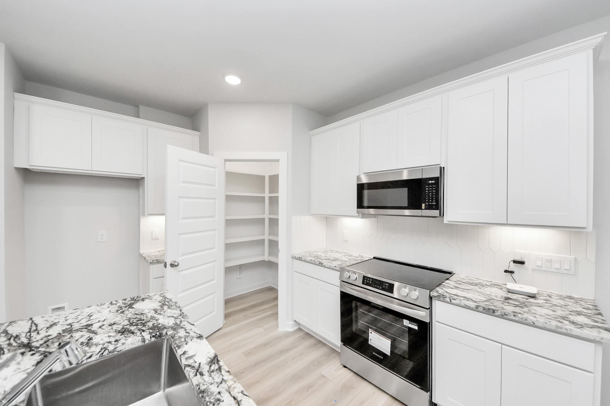 Modern kitchen with white cabinets, granite countertops, and walk-in pantry in The Sabine F floor plan, Cleveland, Texas.