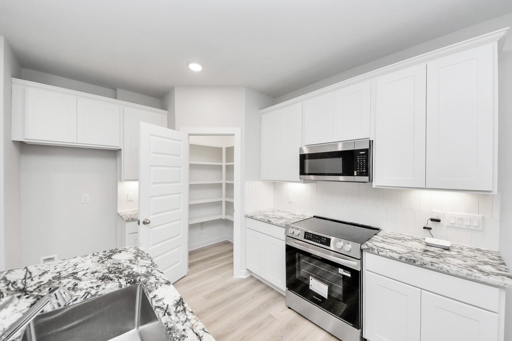 Modern kitchen with white cabinets, granite countertops, and walk-in pantry in The Sabine F floor plan, Cleveland, Texas.