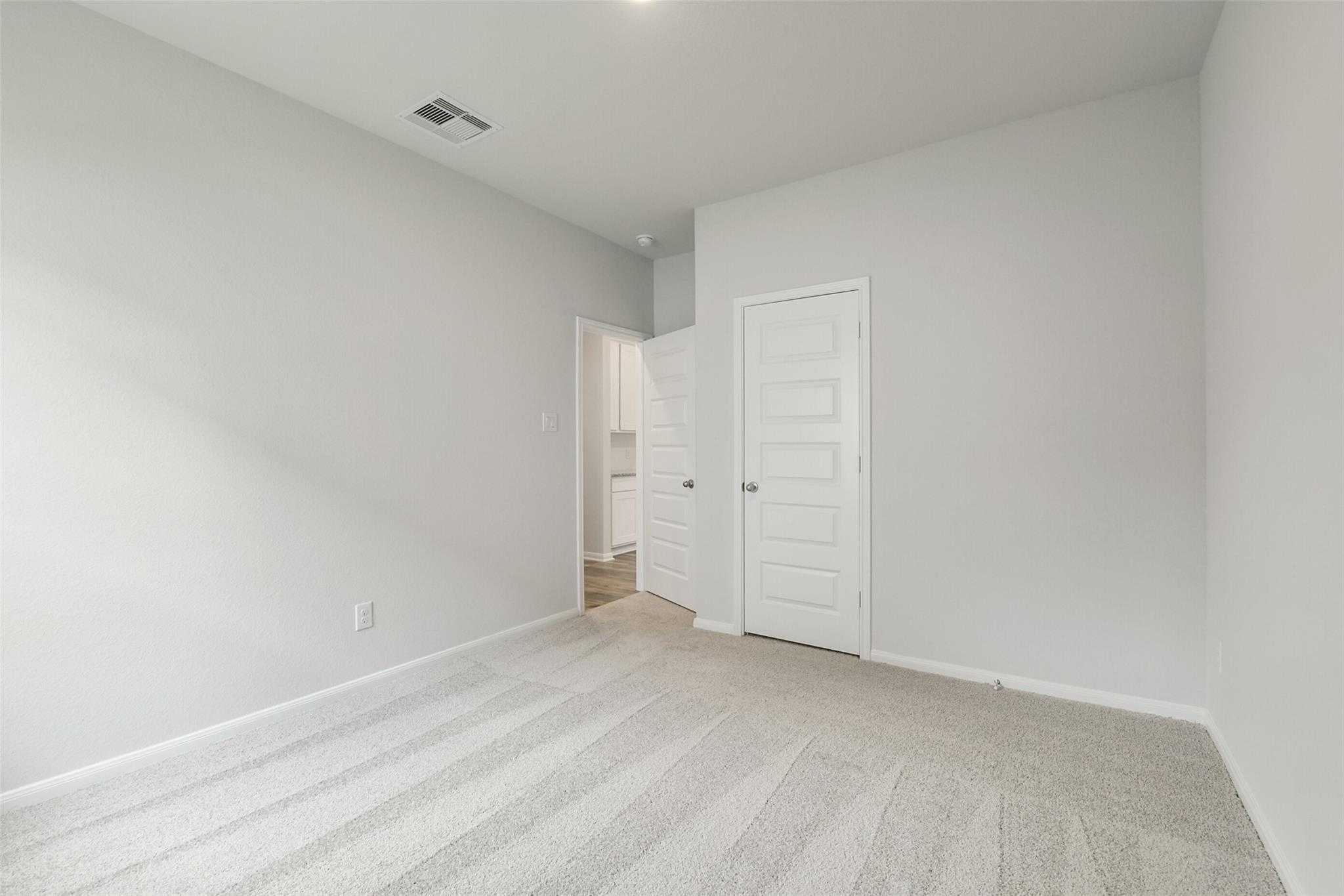 Spacious bedroom with attached bath, light gray walls, plush carpet flooring in Davidson Homes The Frio G, Conroe, Texas
