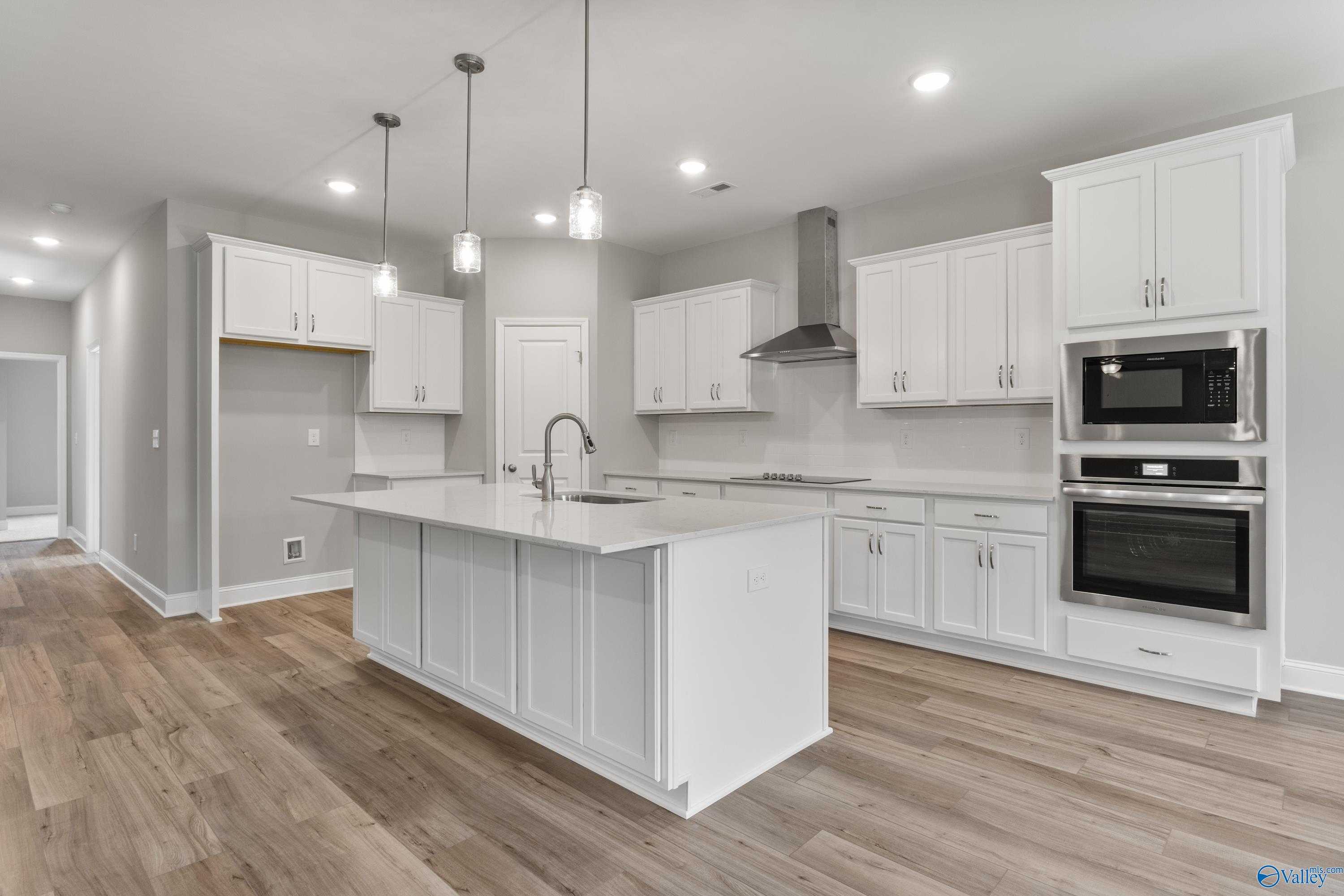 Spacious white kitchen with quartz island sink, stainless double ovens, shaker cabinets, and hardwood floors in Davidson Homes The Rockford, Harvest, AL