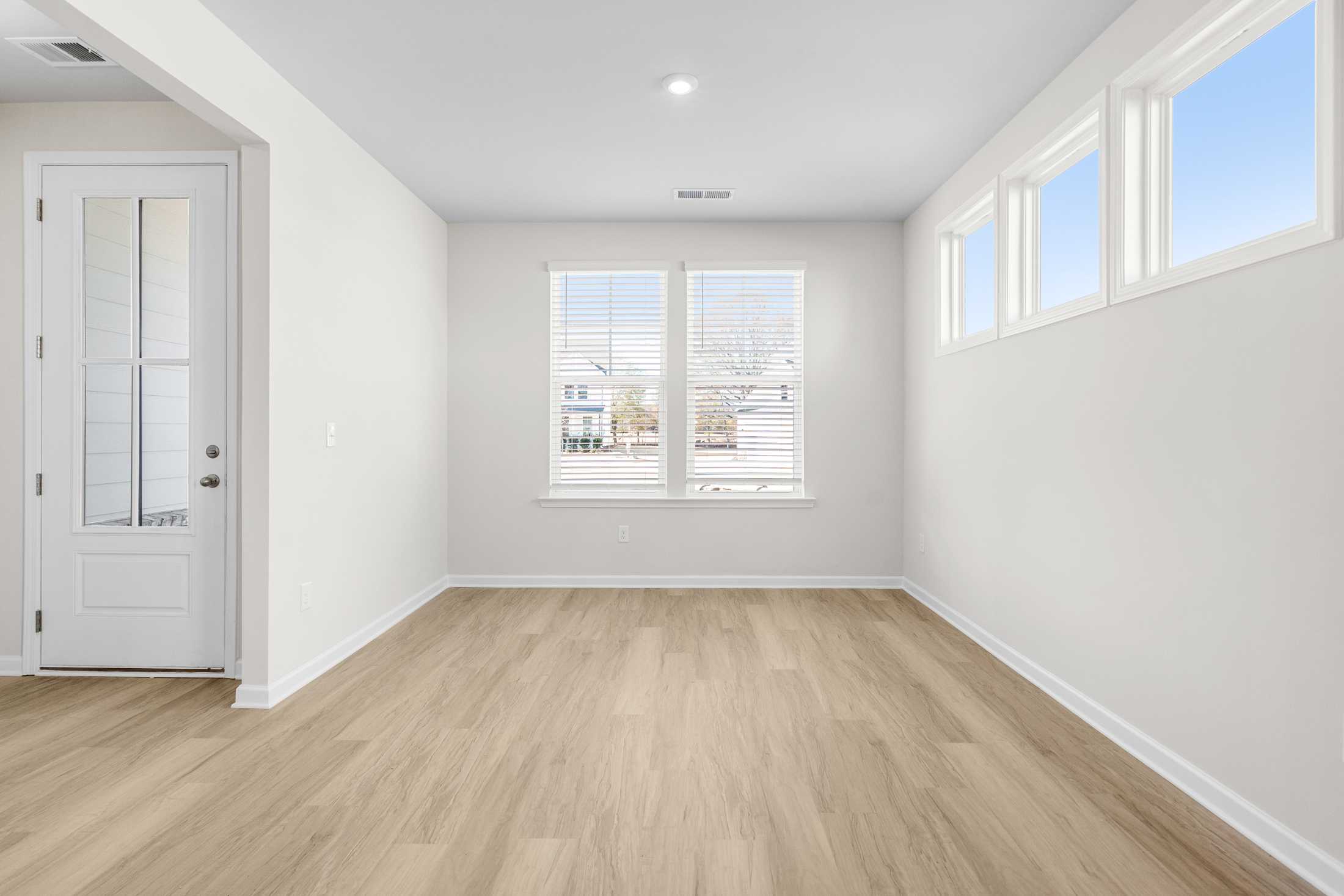 Spacious master bedroom in The Glenwood A at Wehunt Meadows featuring light oak floors, white walls, and large windows with natural light
