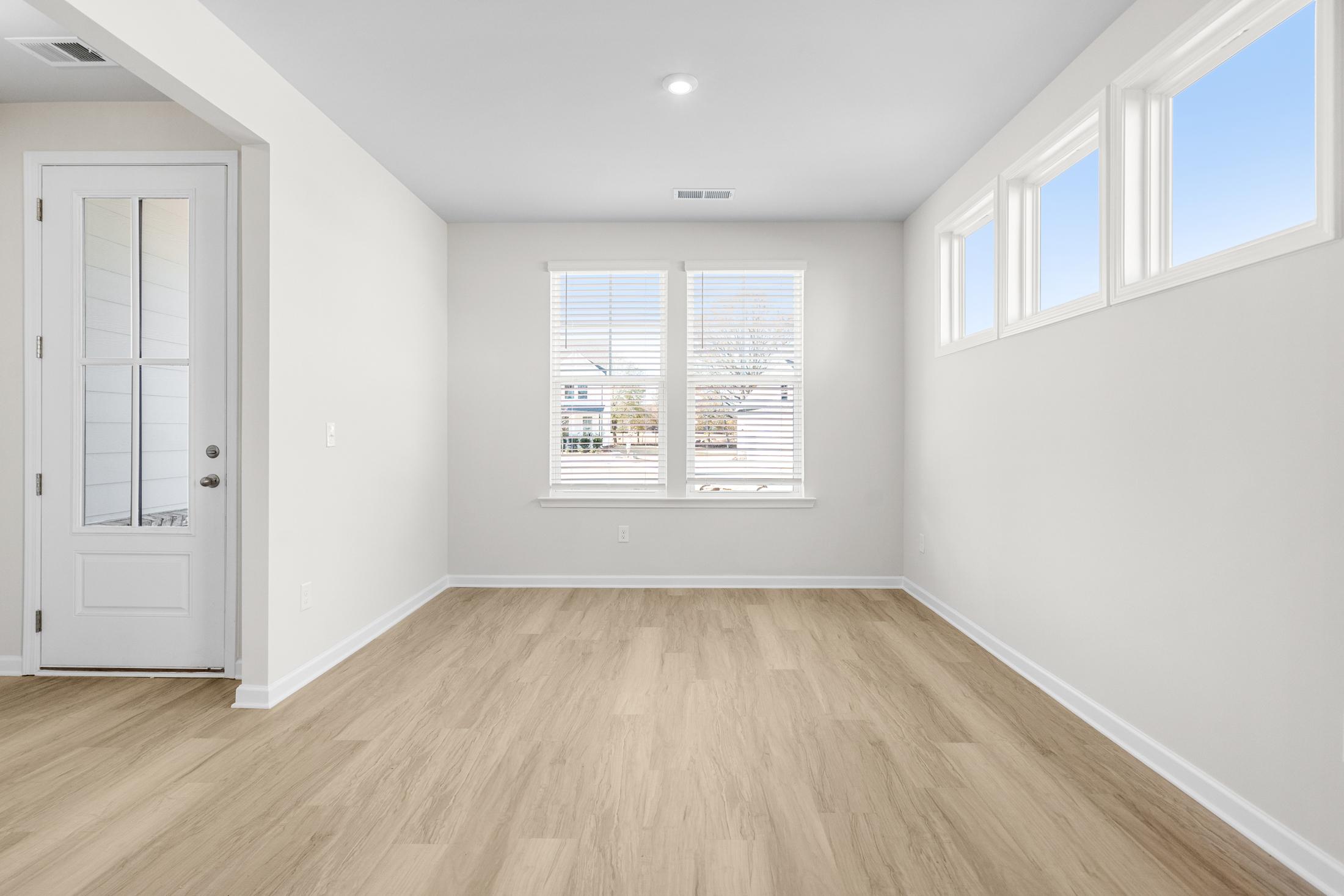 Spacious master bedroom in The Glenwood A at Wehunt Meadows featuring light oak floors, white walls, and large windows with natural light