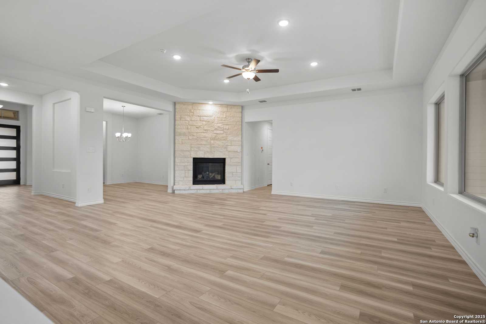 Spacious living room with stone gas fireplace, ceiling fan, and hardwood floors in Davidson Homes Summerlin B, Castroville Texas
