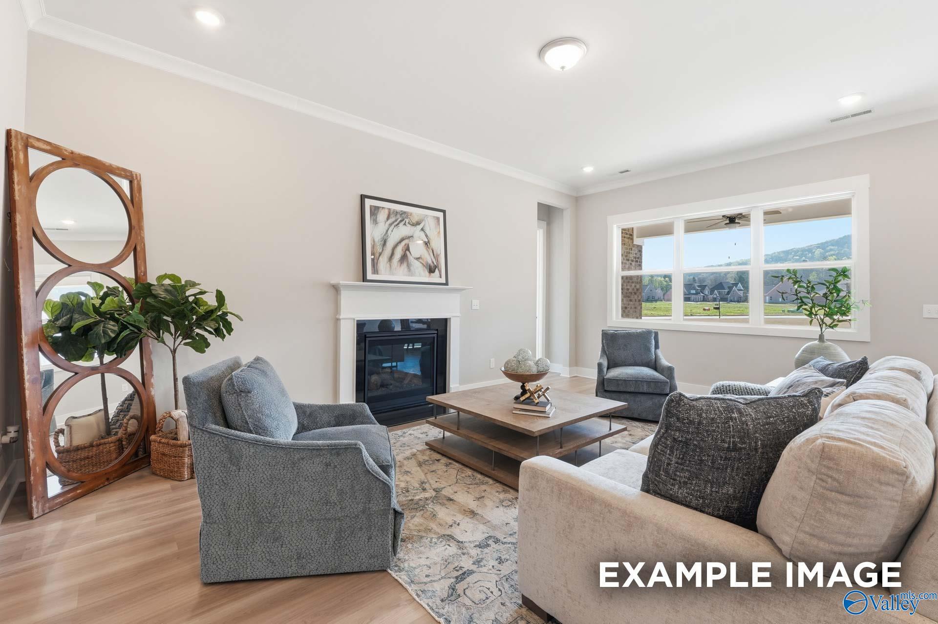 Cozy living room with gas fireplace, beige sectional sofa, blue armchairs, mountain views through large windows in Evermore Homes The Oxford B, Owens Cross Roads, Alabama