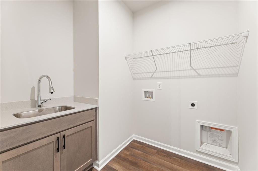 Modern laundry room with utility sink, shaker cabinets, wire shelving, and washer-dryer hookups in The Glenwood A by Davidson Homes, Loganville, GA