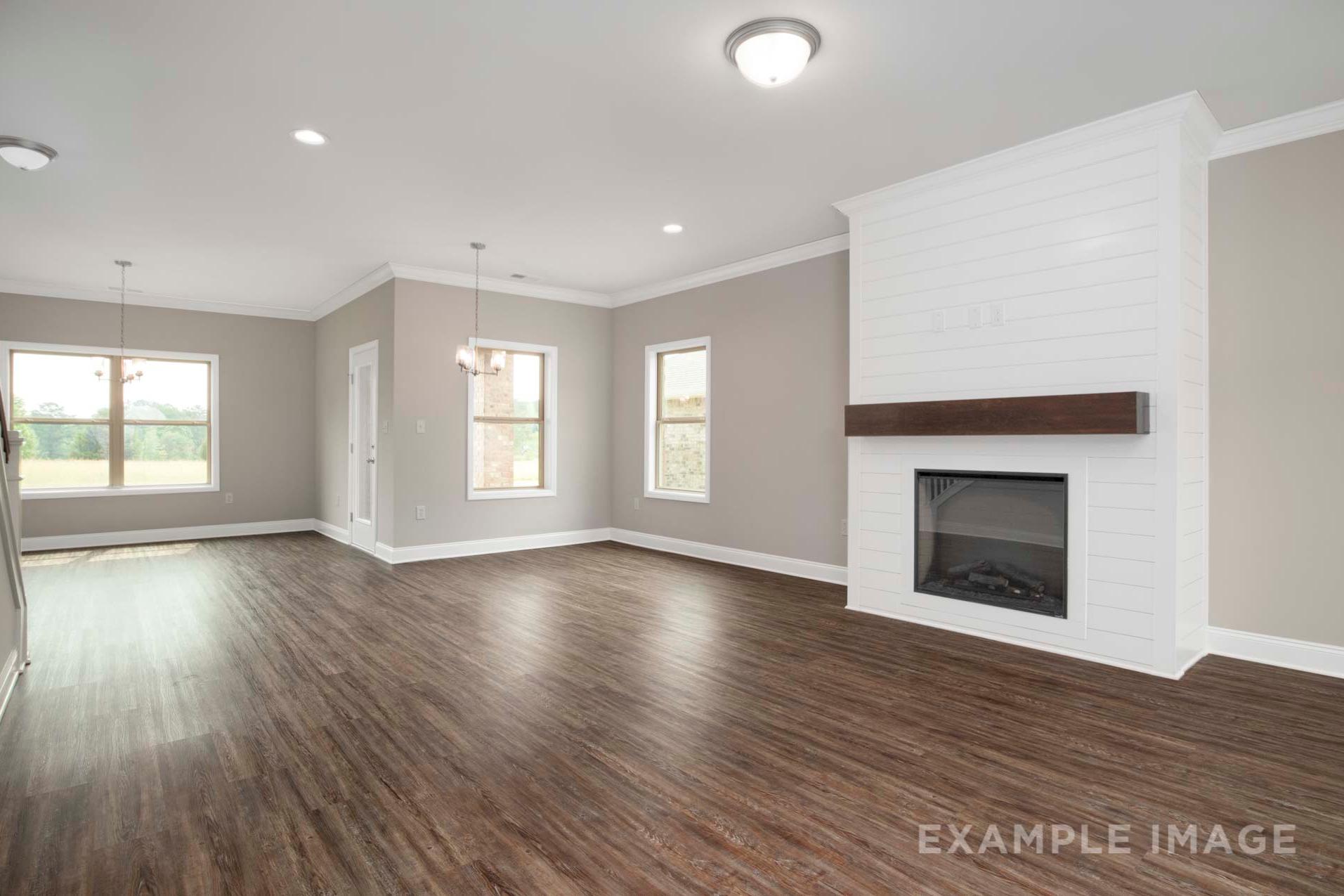 Spacious open-concept living room in The Charleston D with shiplap gas fireplace, hardwood floors, and large windows