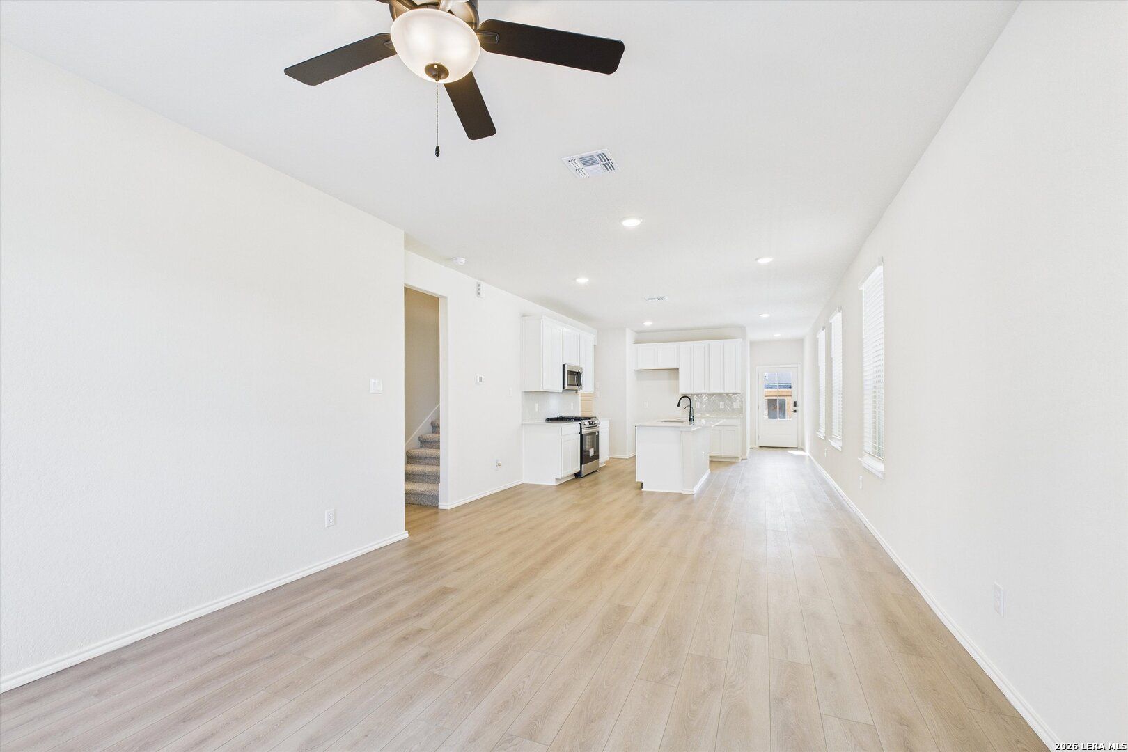 Open kitchen-living space with white cabinets, center island, ceiling fan, and hardwood floors in Davidson Homes The Gillian B, San Antonio