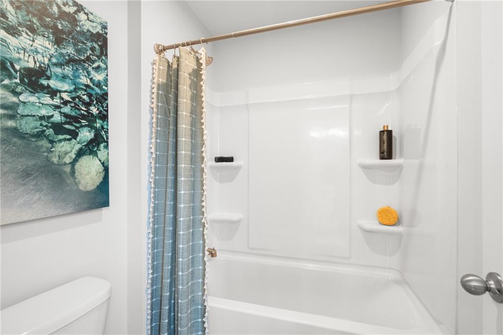 Modern white bathtub with blue-gray shower curtain and built-in shelves in The Wilmington B bathroom, Davidson Homes, Stegall Village, Emerson, Georgia