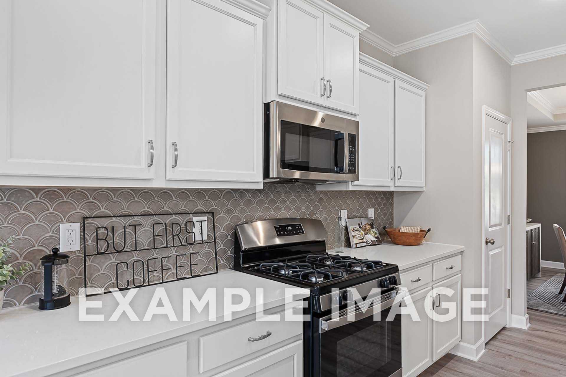 Modern kitchen in The Ash E home featuring white shaker cabinets, stainless steel appliances, and scalloped gray backsplash