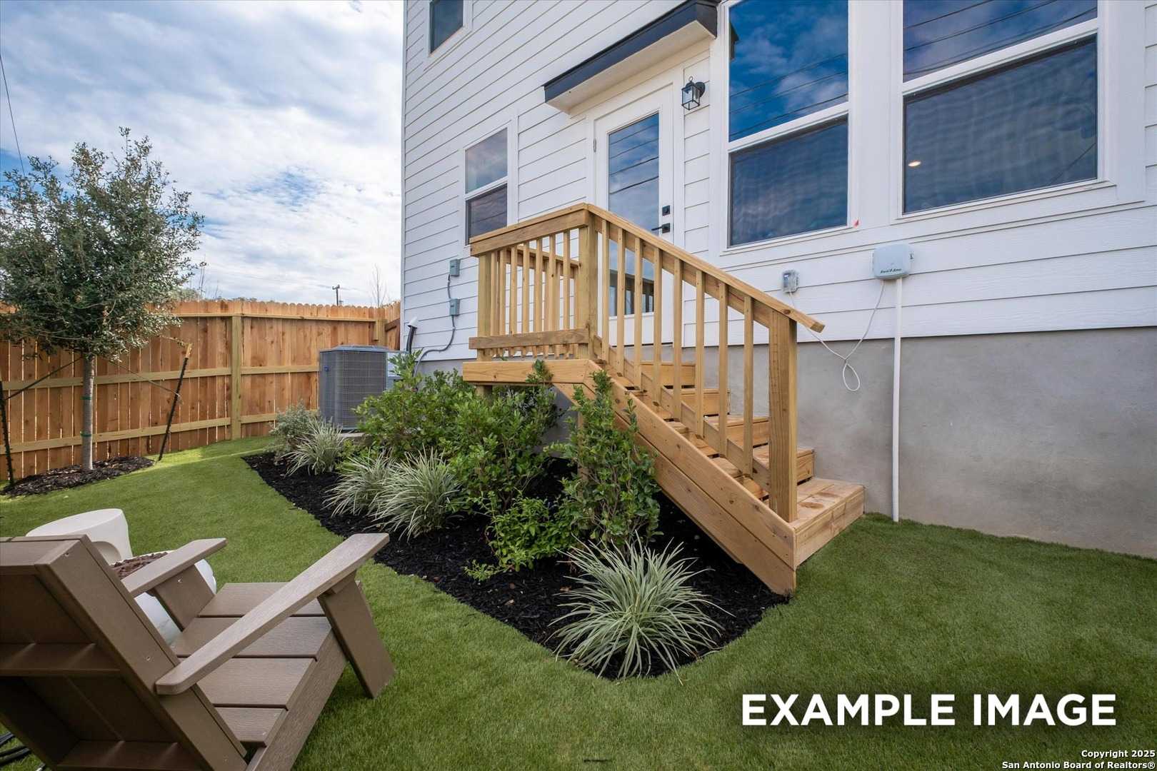 Landscaped backyard with wooden deck stairs to two-story white home, synthetic turf, Adirondack chairs, and privacy fence in Meadows at Oak Creek, San Antonio