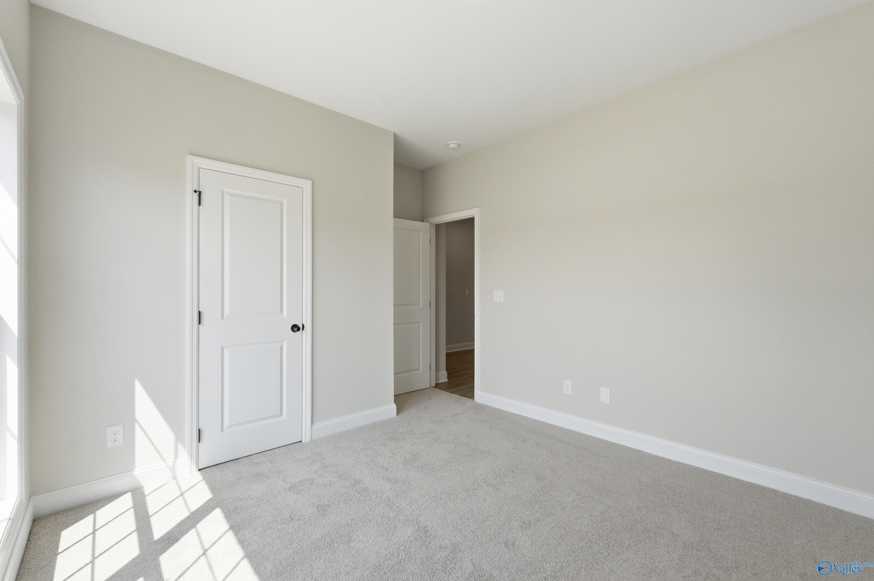 Bright bedroom featuring light gray walls, white doors, gray carpet, and natural sunlight in Davidson Homes The Franklin C, Meridianville Alabama
