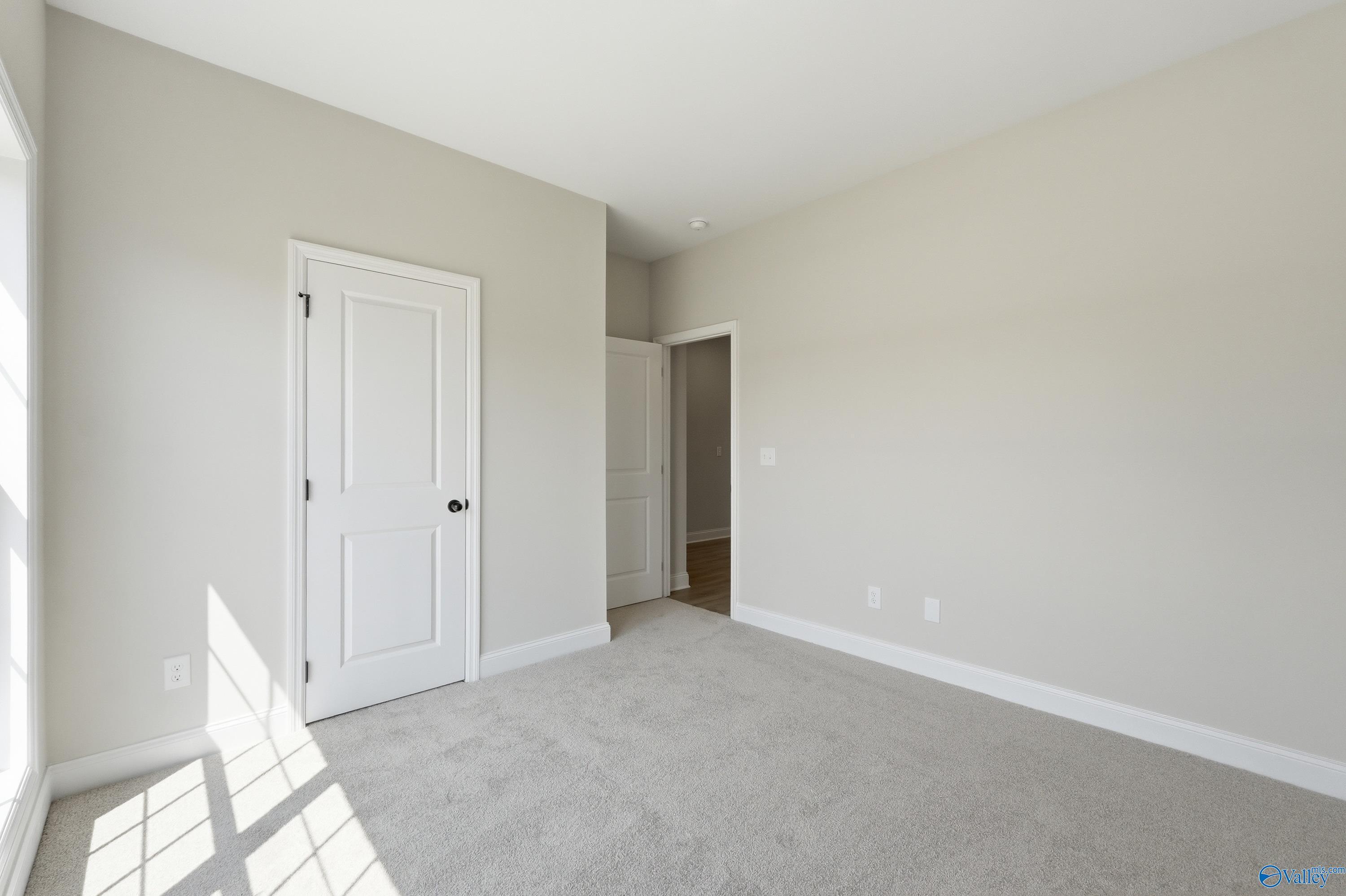 Bright bedroom featuring light gray walls, white doors, gray carpet, and natural sunlight in Davidson Homes The Franklin C, Meridianville Alabama