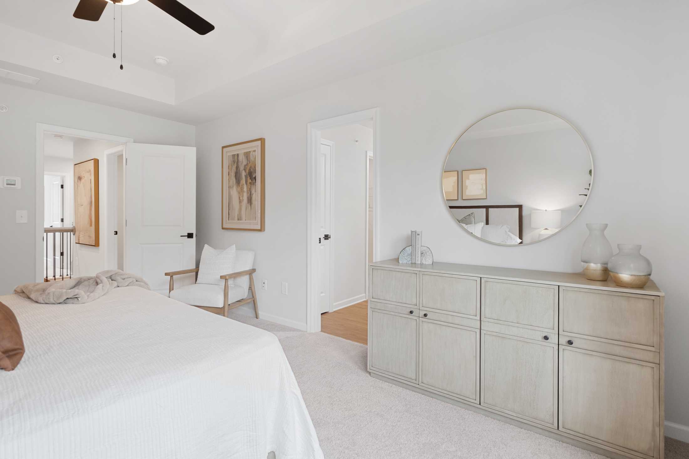 Serene bedroom interior at Rosehill Townhomes in Marietta GA with white bedding, round mirror, ceiling fan, and white dresser