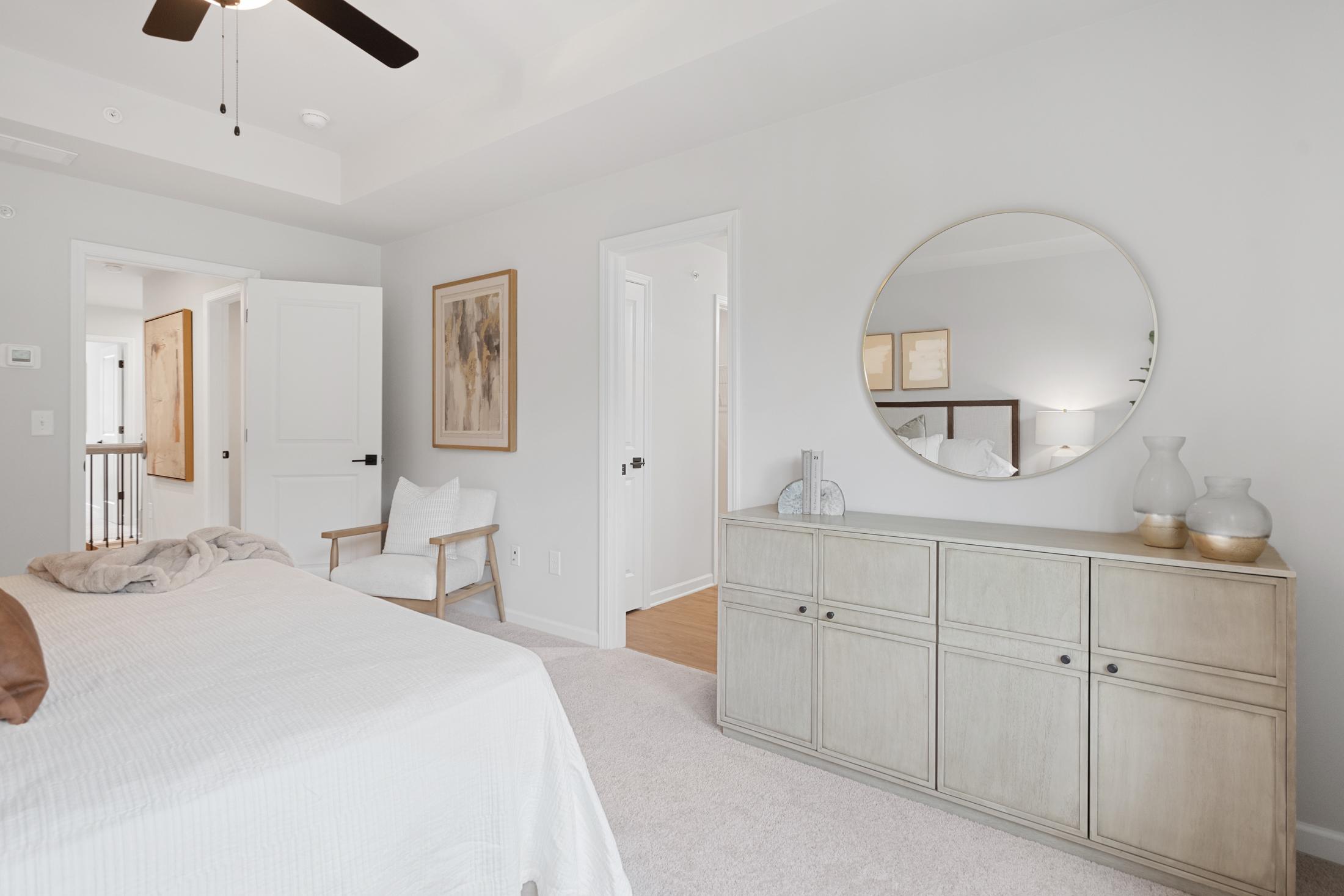 Serene bedroom interior at Rosehill Townhomes in Marietta GA with white bedding, round mirror, ceiling fan, and white dresser