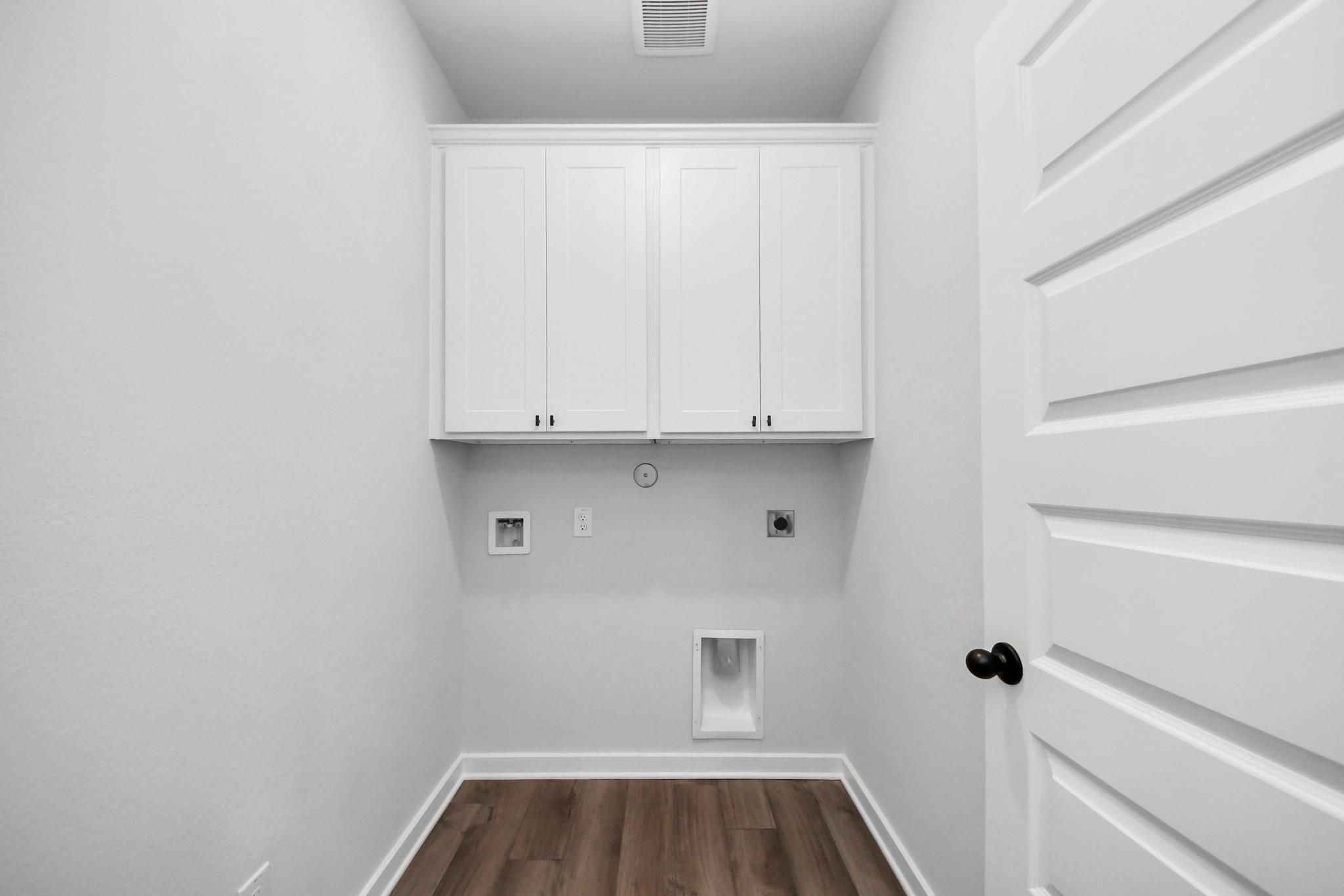 Laundry room with white cabinets and wood-look flooring in The Riviera C floor plan at River Ranch Meadows, Dayton, Texas.