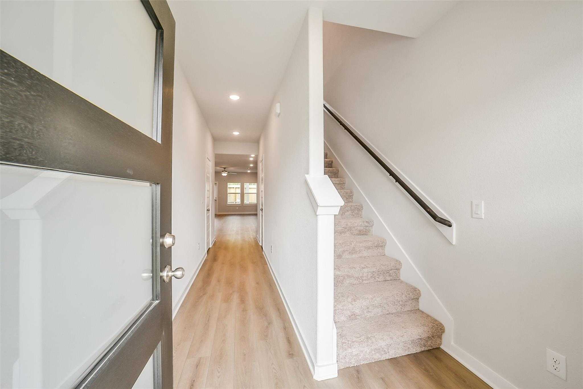 Bright entry hallway with open glass door, light wood floors, white walls, and carpeted staircase in Davidson Homes The Blanco E, Magnolia Texas