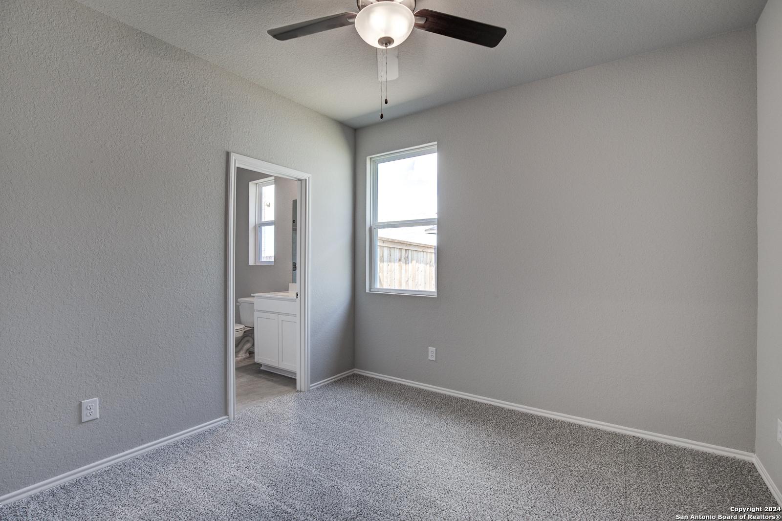 Cozy gray bedroom with ceiling fan, window, and en-suite bath in Davidson Homes The Daphne J, Seguin, Texas