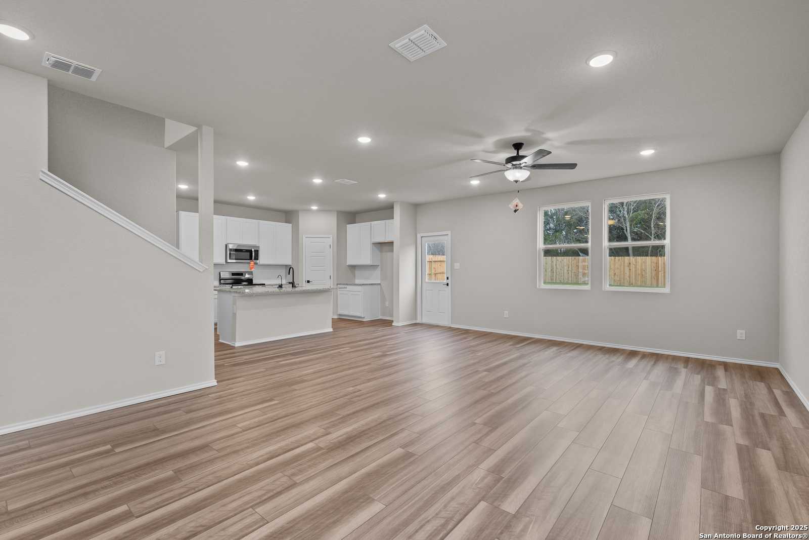 Open-concept living and kitchen with white cabinets, hardwood floors, ceiling fans, and large windows in Davidson Homes The Murray I, San Antonio