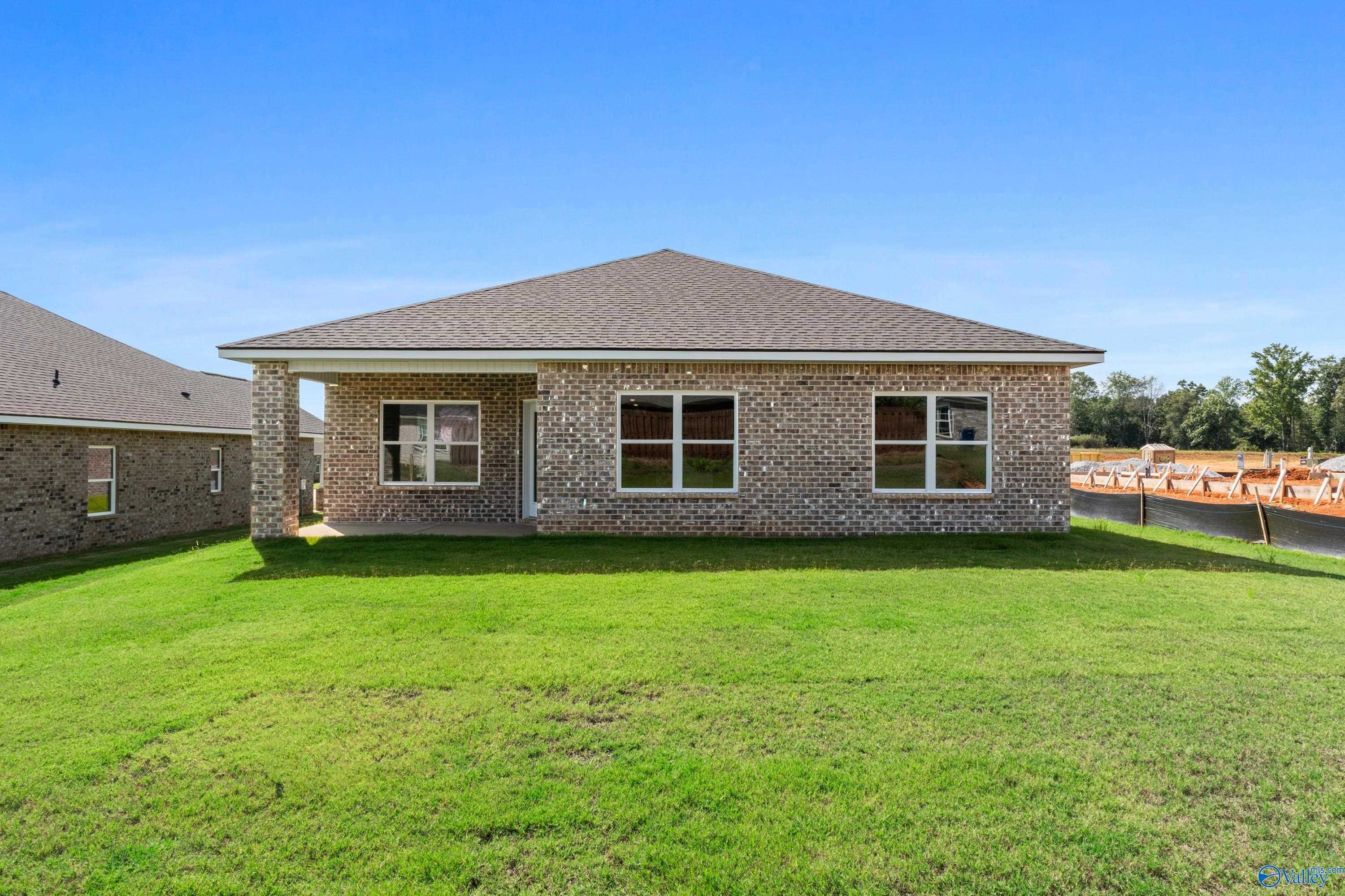 Single-story brick home with gabled roof, covered porch, double windows, and lush green lawn in Wood Trail, Toney, Alabama