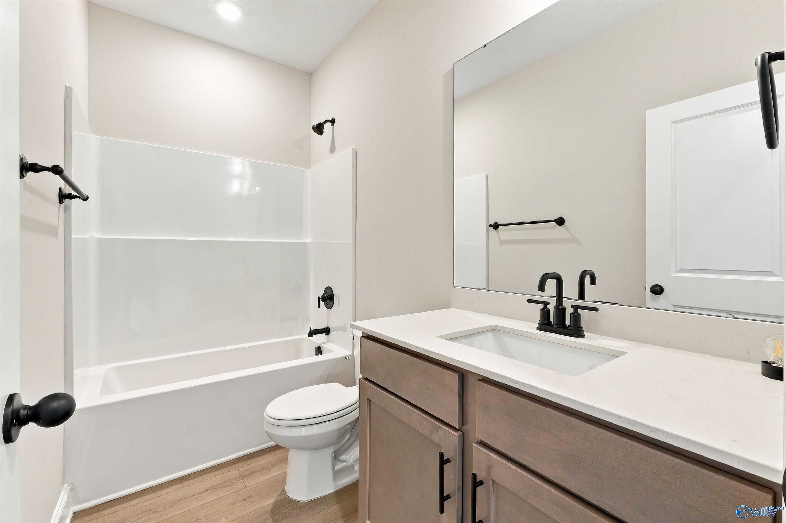 Modern bathroom with tub-shower combo, matte black fixtures, quartz vanity, and wood-look flooring in Davidson Homes' Franklin C plan, Athens, AL