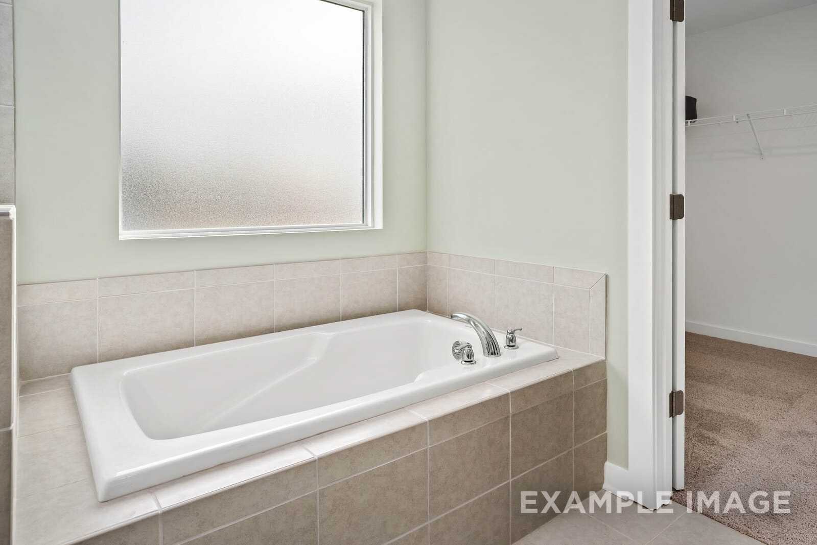 Spacious master bathroom in The Gordon B showcasing white soaking tub, beige tile surround, and frosted window