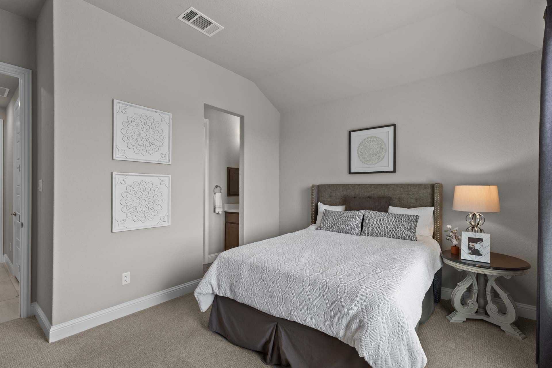 Cozy bedroom with gray walls, upholstered queen bed, white bedding, framed art, and en-suite bath at Ladera San Antonio by Davidson Homes