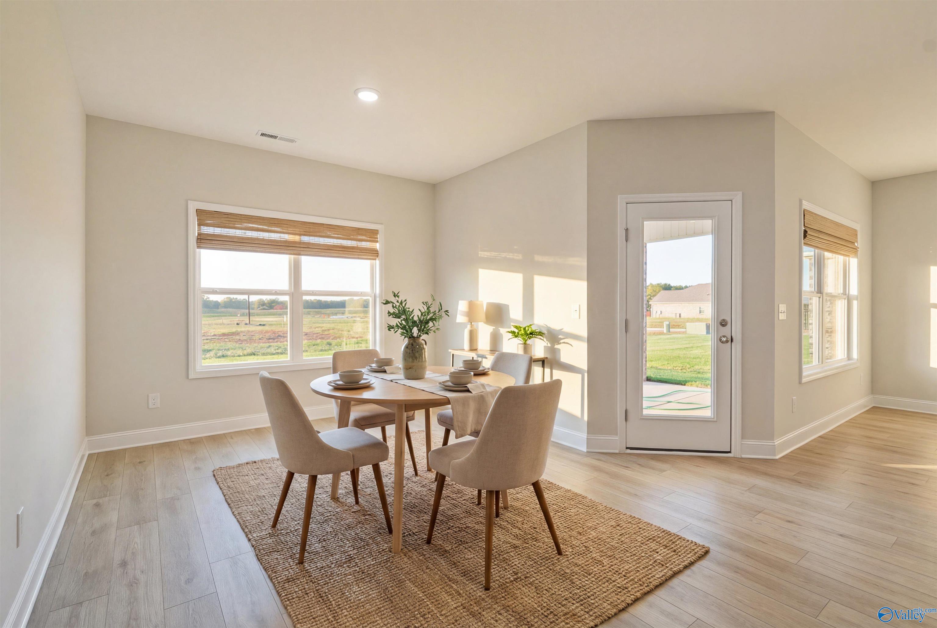 Bright dining room with round wooden table, beige chairs on seagrass rug, large windows and glass door to rural backyard in The Everett floor plan, Hazel Green, Alabama