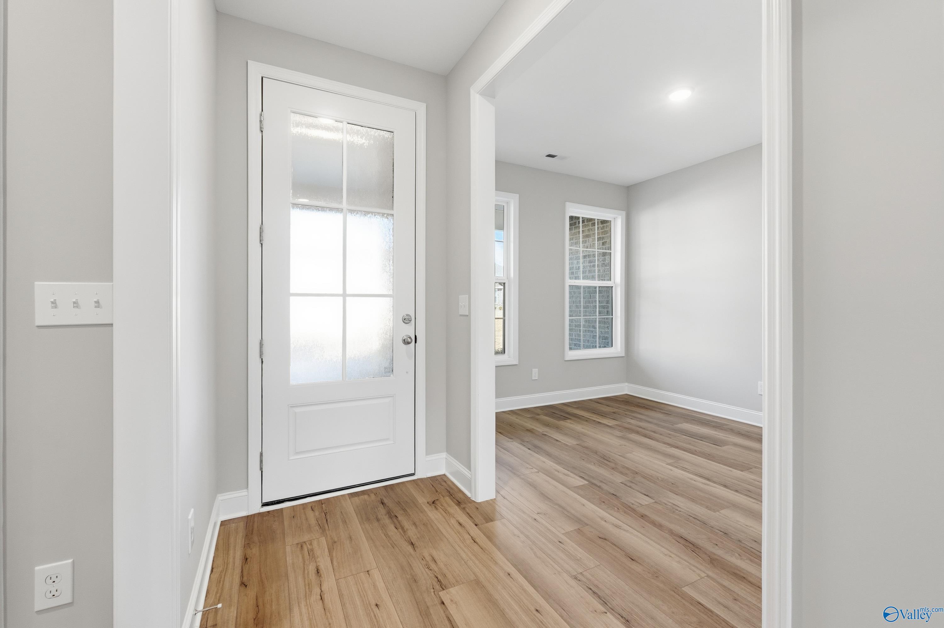 Bright entryway with white glass-paneled door, light gray walls, and hardwood floors in Davidson Homes The Rockford, Creekside, Harvest, AL