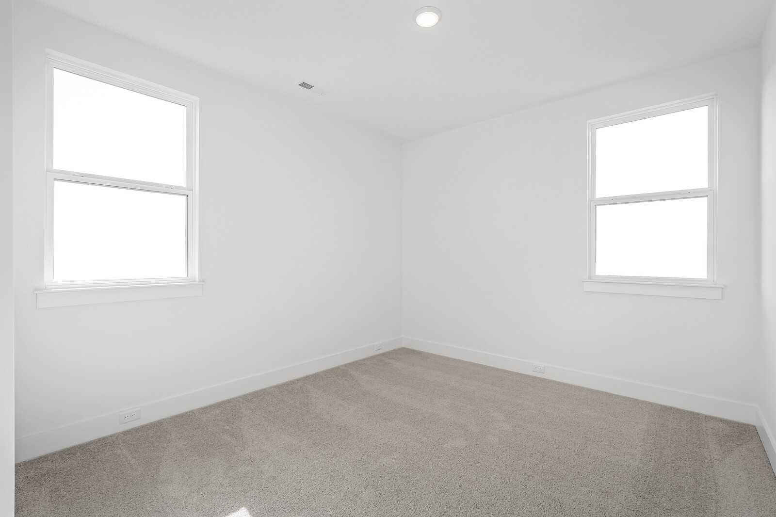 Bright empty bedroom with double-hung windows, white walls, and beige carpet in Davidson Homes The Alston A, Murfreesboro