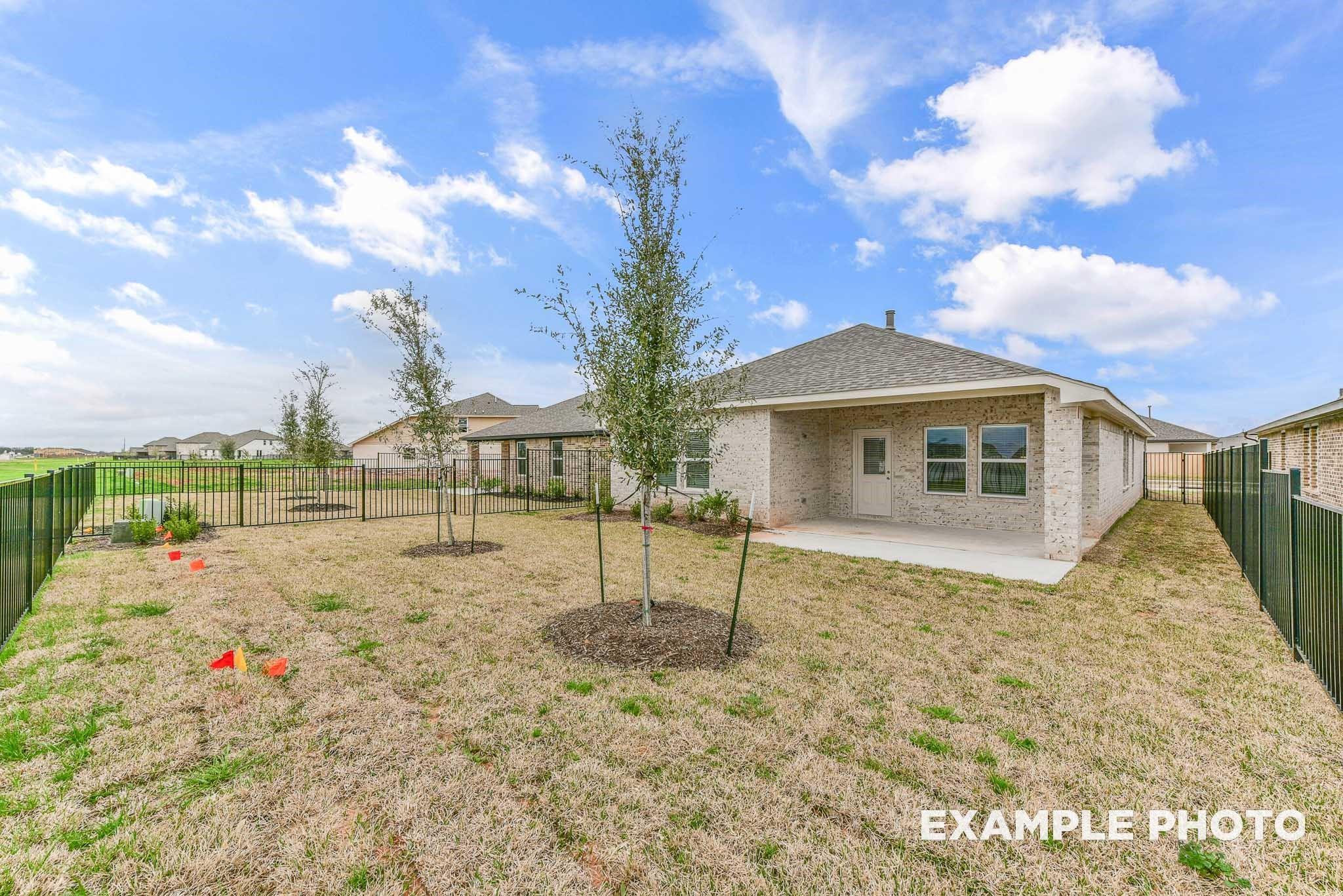 Covered back patio and spacious backyard with young trees, black fence in Davidson Homes Riviera A, Sierra Vista, Rosharon, Texas