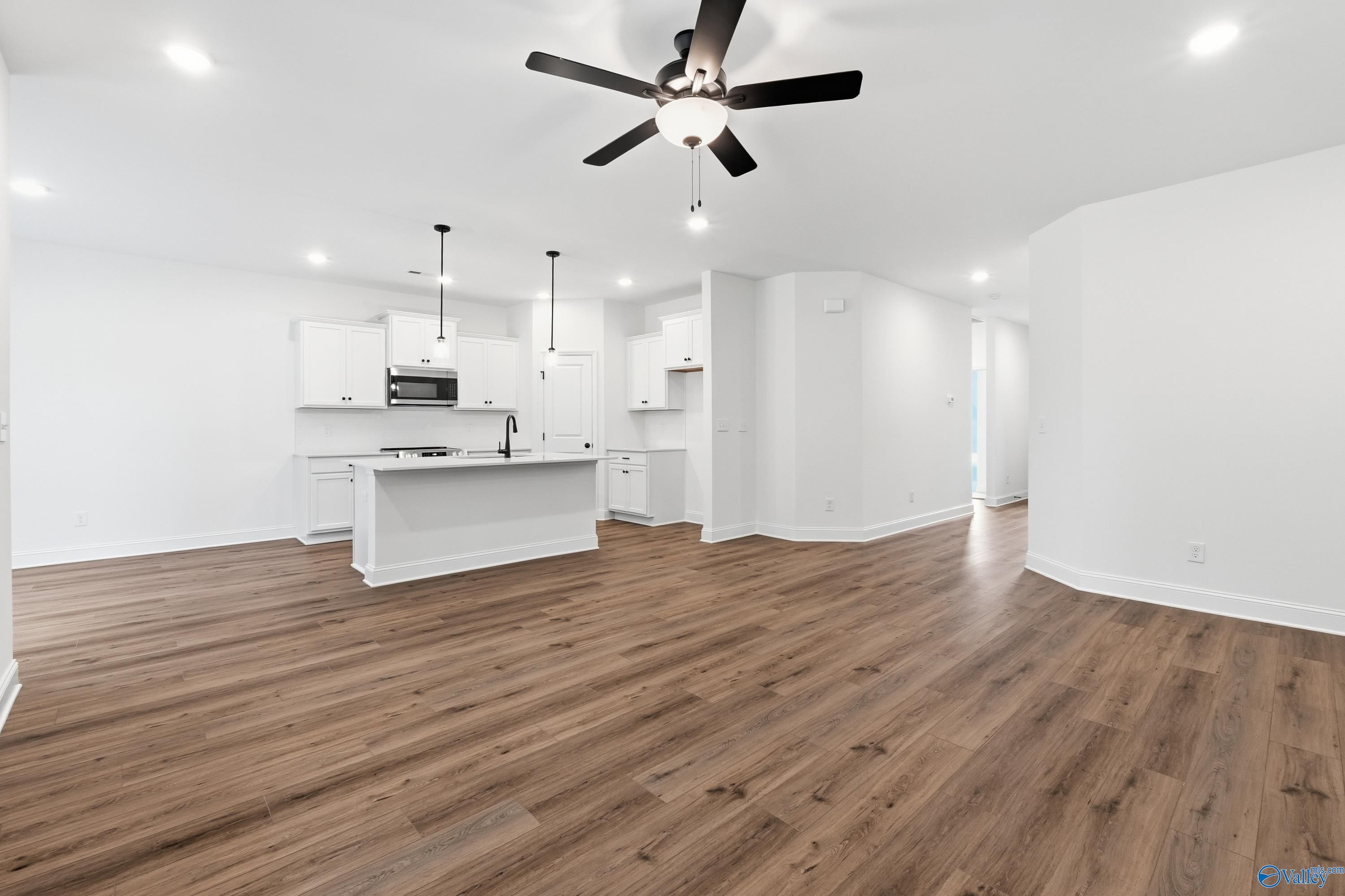 Bright open-concept kitchen with white cabinets, stainless appliances, island, and hardwood floors in Davidson Homes The Asheville C, Arab, AL