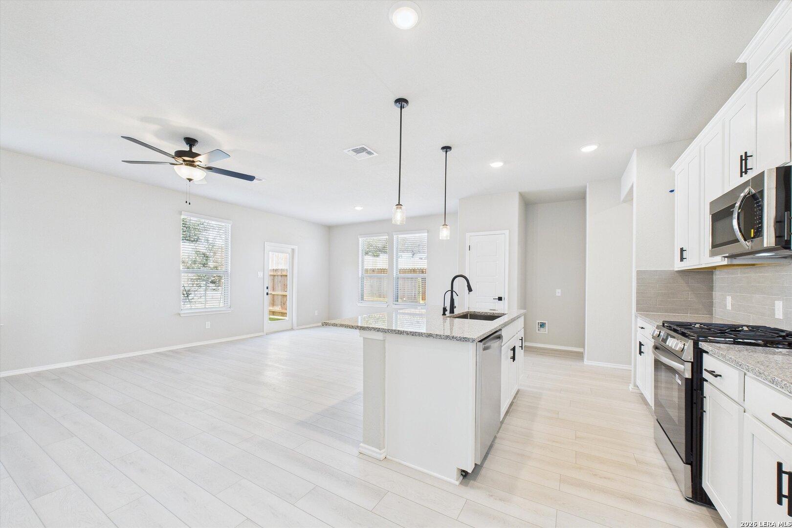 Modern open-concept kitchen with white cabinets, stainless appliances, and pendant lights in Davidson Homes The Charlotte A, San Antonio, Texas
