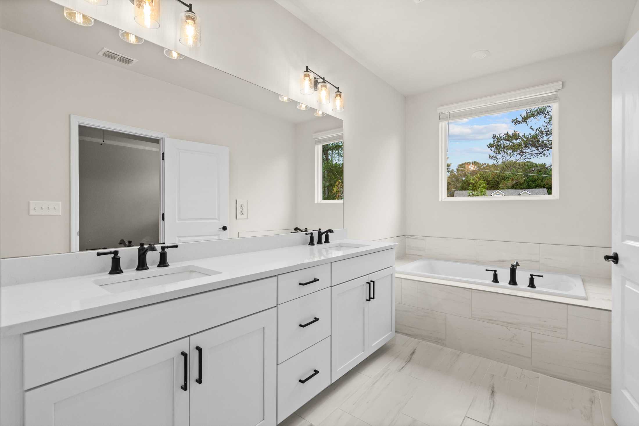 Spacious master bathroom in The Glenwood B featuring double vanity, soaking tub, and natural light window