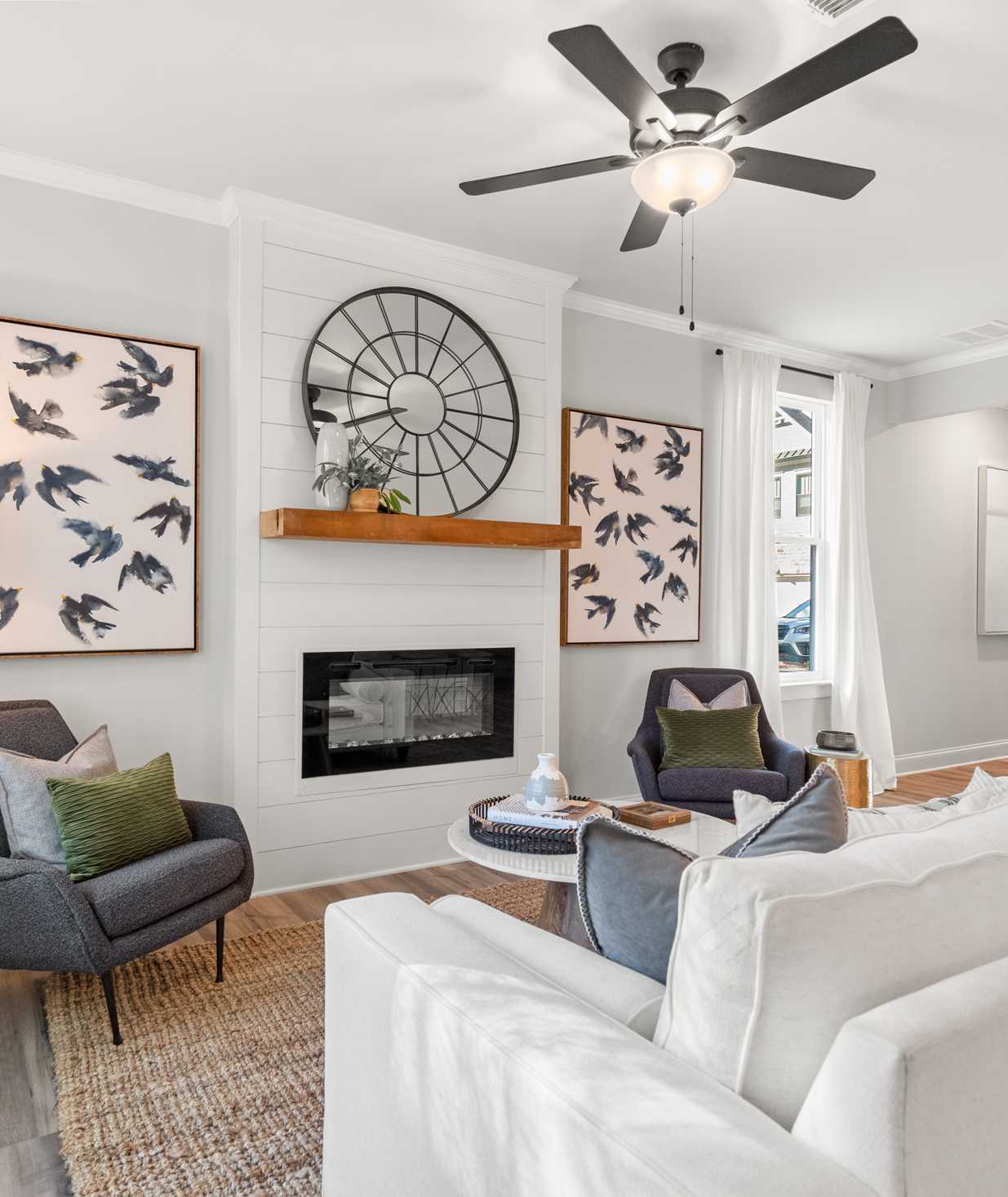 Modern living room with gas fireplace, white sofas, bird art, and ceiling fan at The Village at Towne Lake, Woodstock GA by Davidson Homes