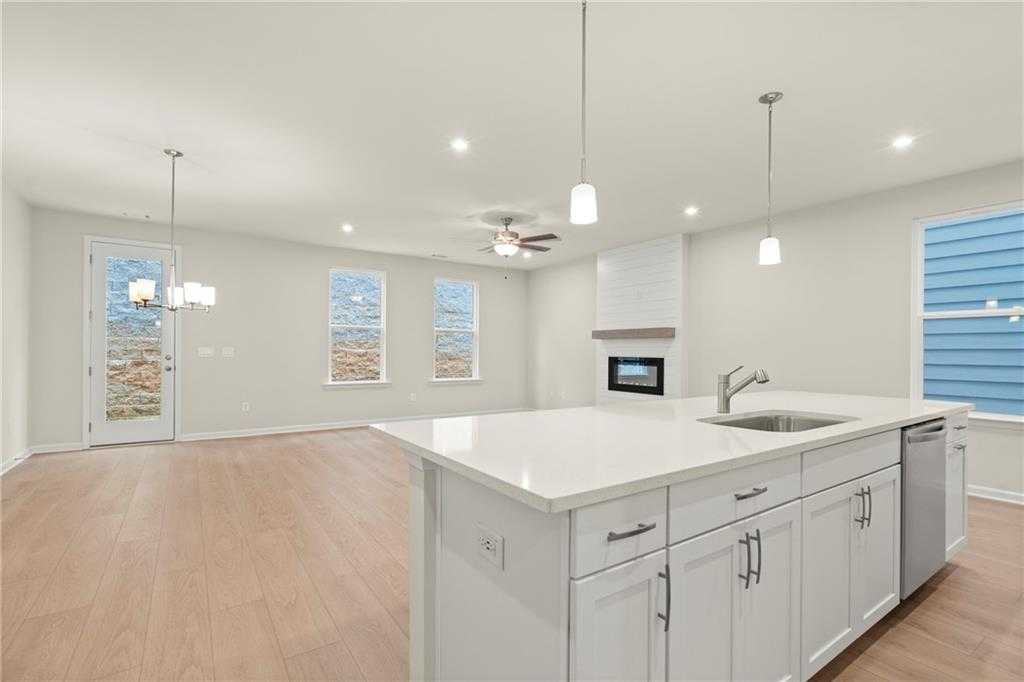 Bright open-concept kitchen-living area with white island sink, gas fireplace, hardwood floors, and large windows in Davidson Homes The Cary A, Kennesaw, GA
