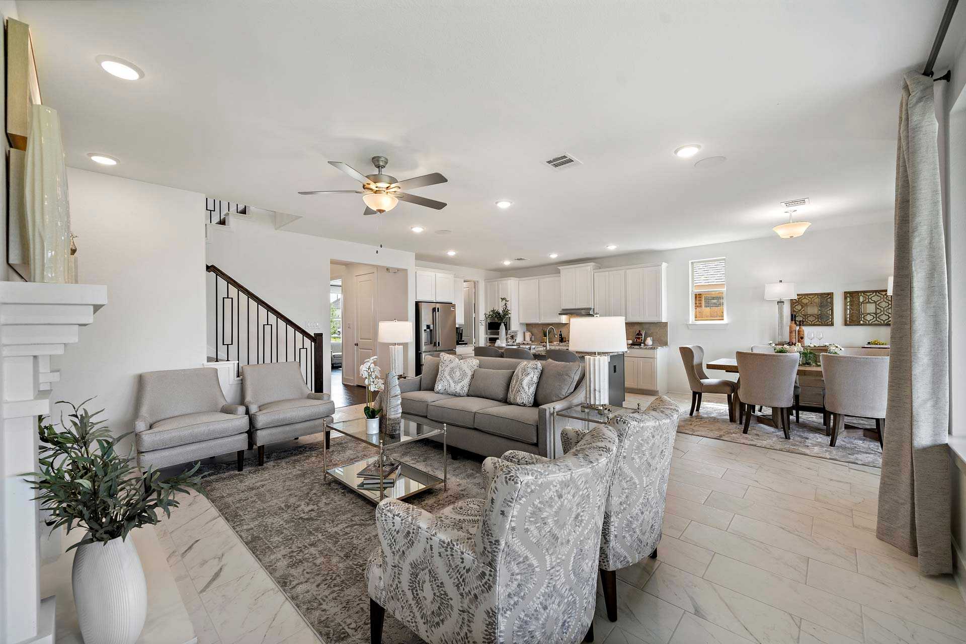Open-concept living room in Sierra Vista Rosharon Texas with gray sectional sofa, fireplace, staircase, and adjacent kitchen dining area