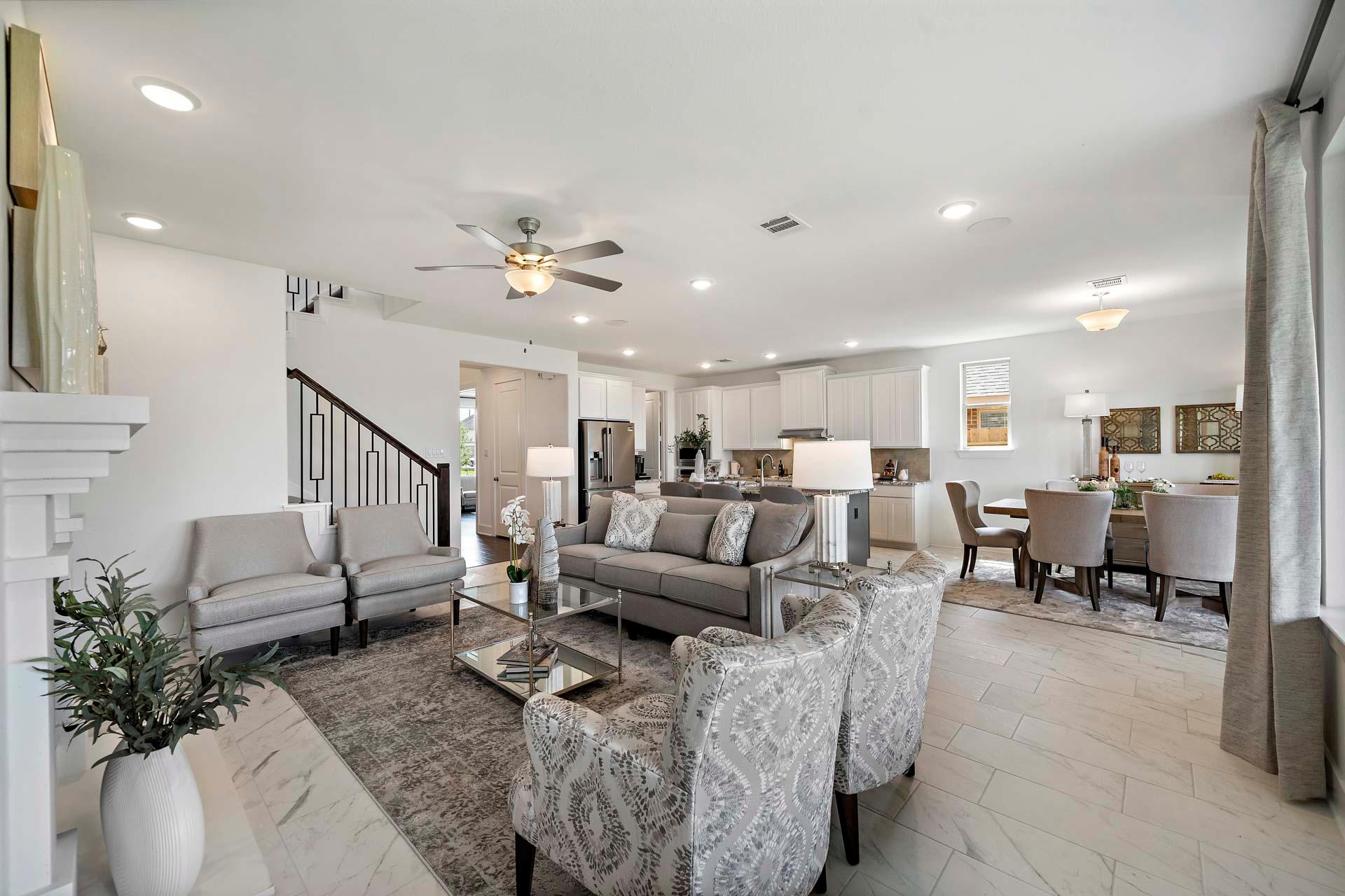 Open-concept living room in Sierra Vista Rosharon Texas with gray sectional sofa, fireplace, staircase, and adjacent kitchen dining area