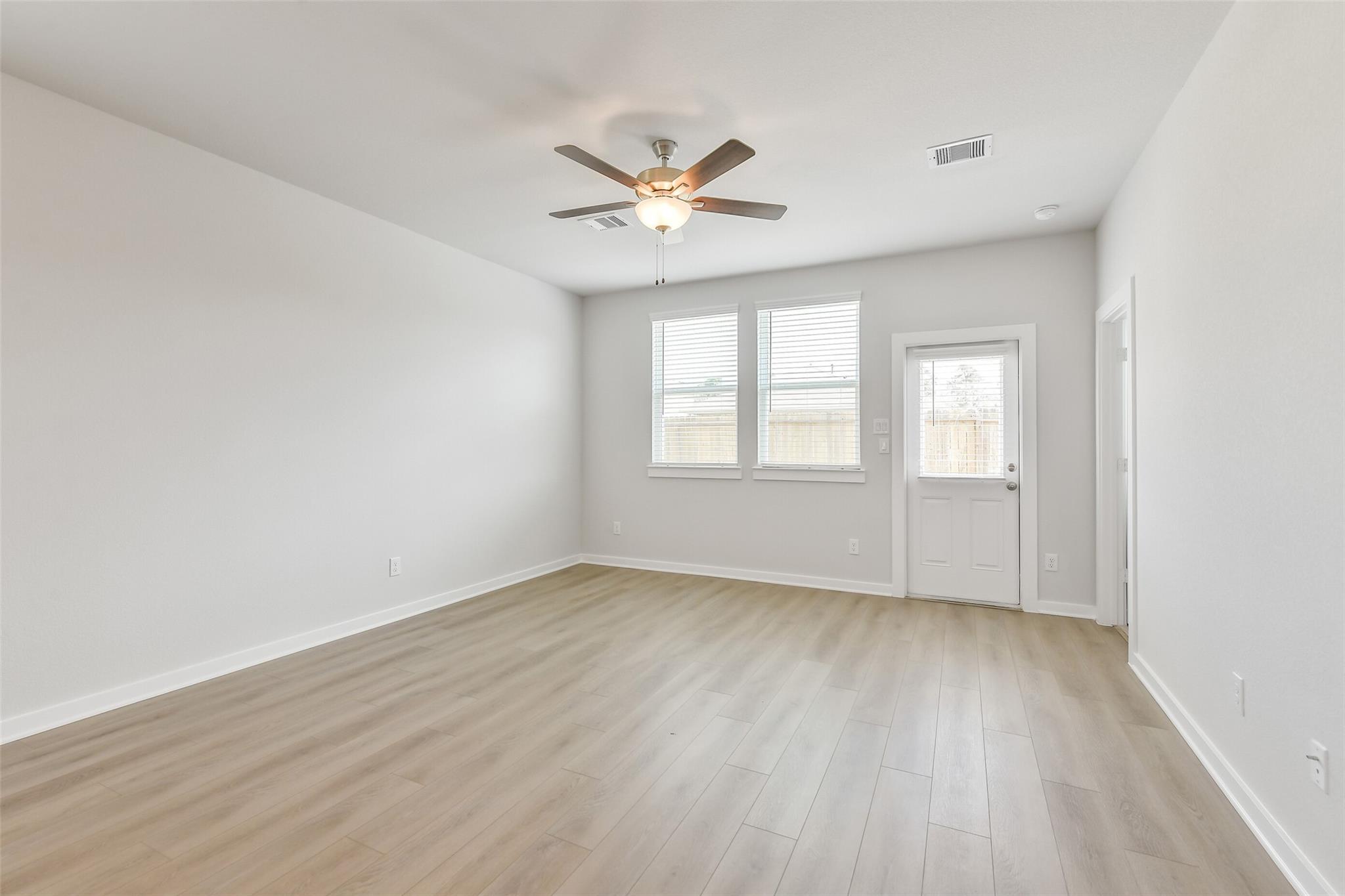Bright living room with ceiling fan, large windows with blinds, and light wood floors in Davidson Homes The Colorado F, Cleveland, Texas