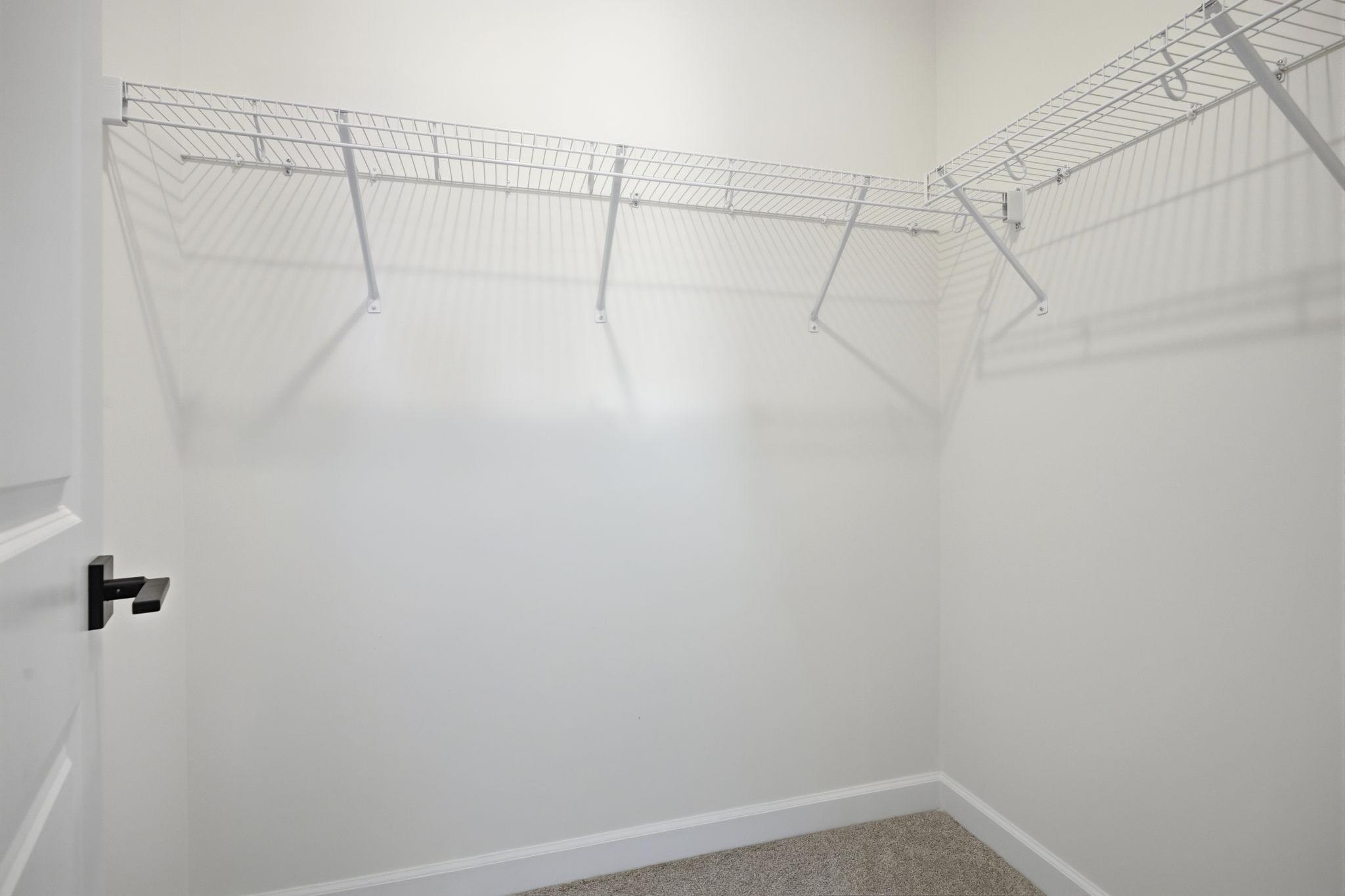 Spacious walk-in closet in The Ashport K home design featuring white wire shelving and plush carpeting.
