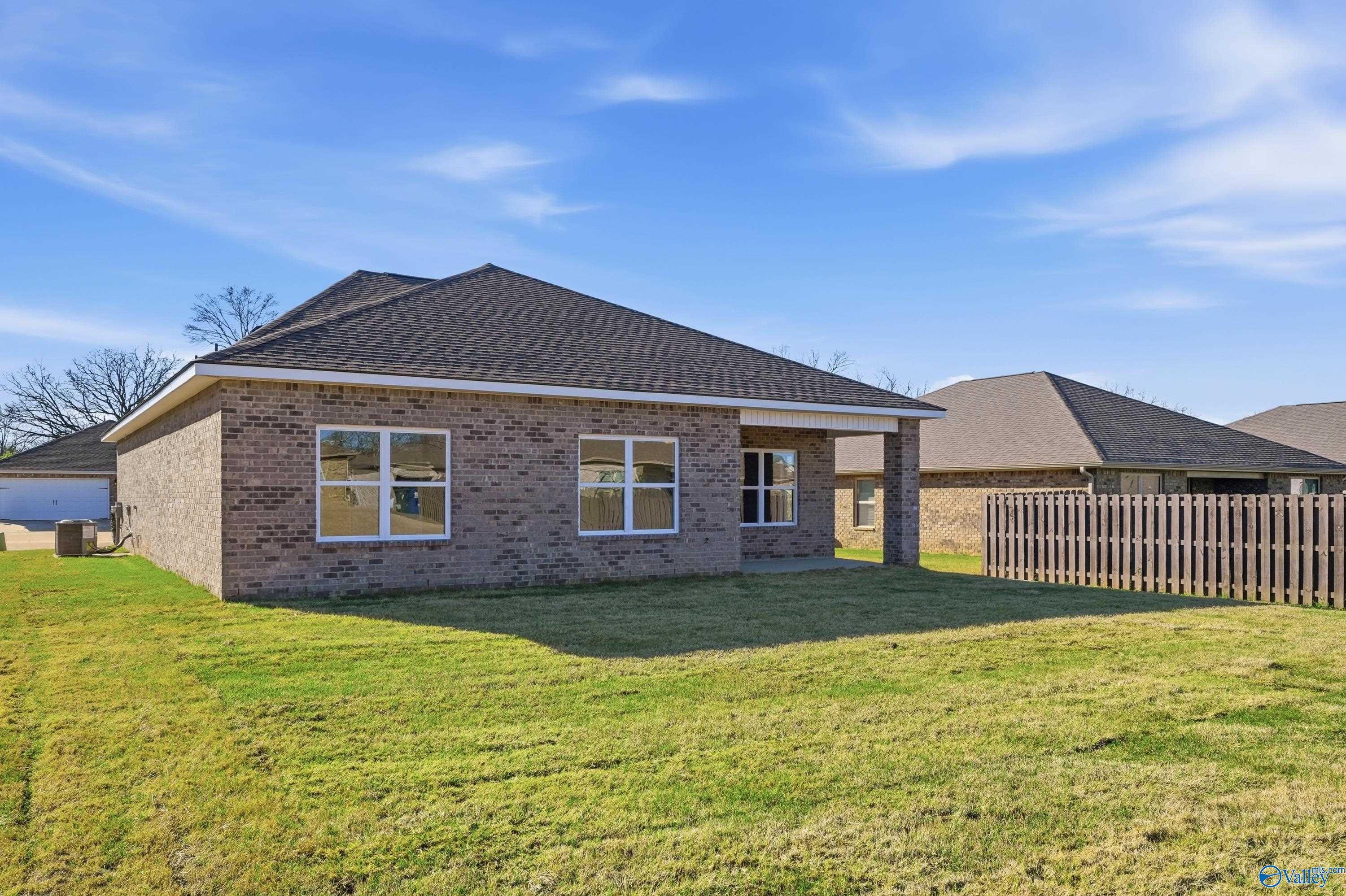 Single-story brick home with shingled roof, large windows, and fenced green yard in Flint Meadows, New Market, Alabama by Davidson Homes