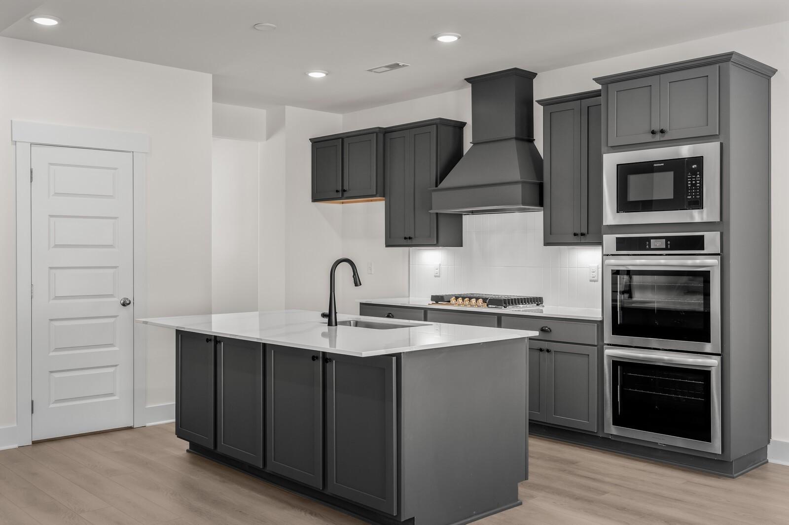 Modern kitchen with dark gray cabinets, quartz island, and stainless steel appliances in The Willow at Woods Crossing.