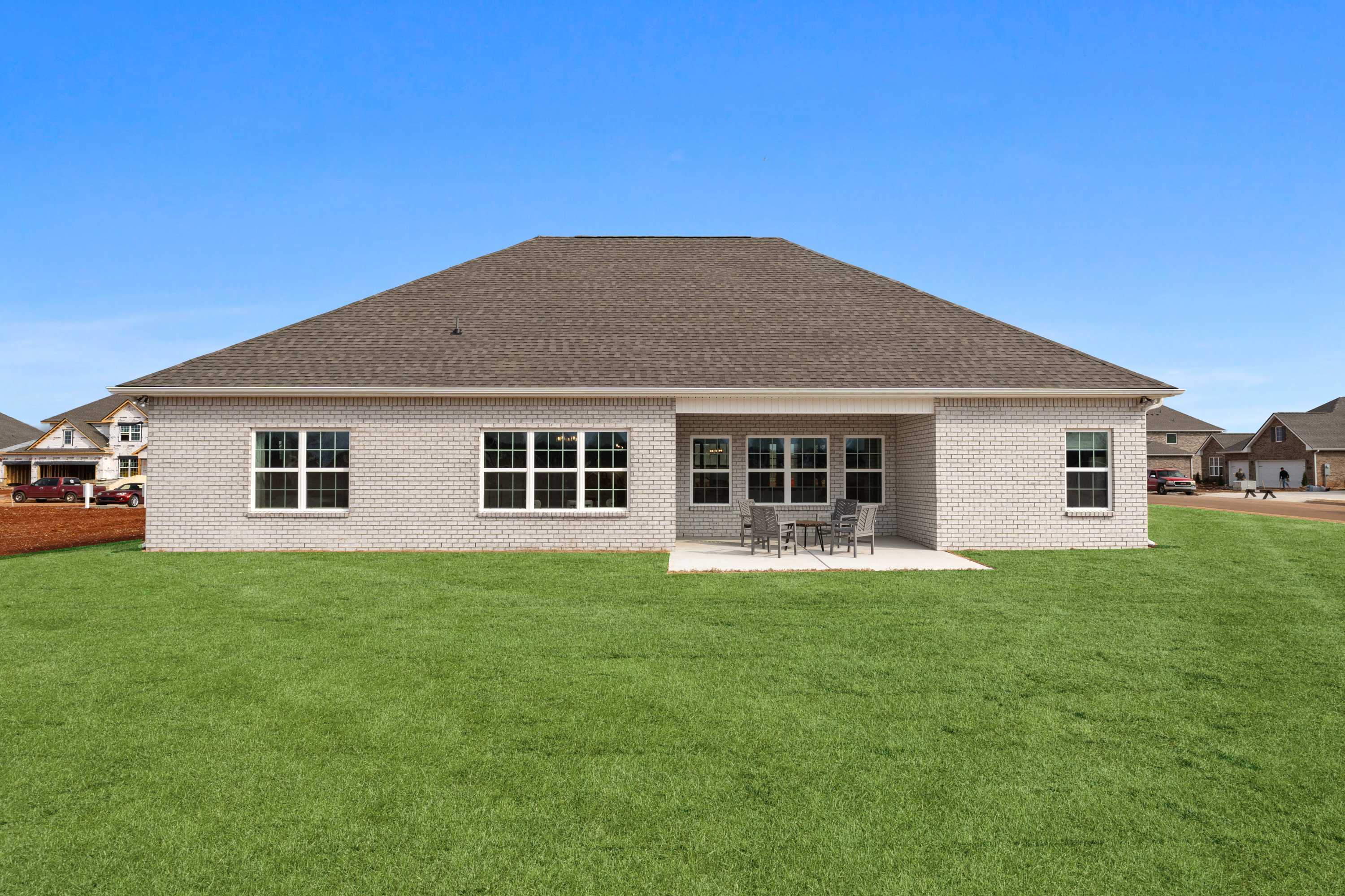 Backyard view of single-story brick home at Briercreek in Meridianville AL with covered patio seating and green lawn