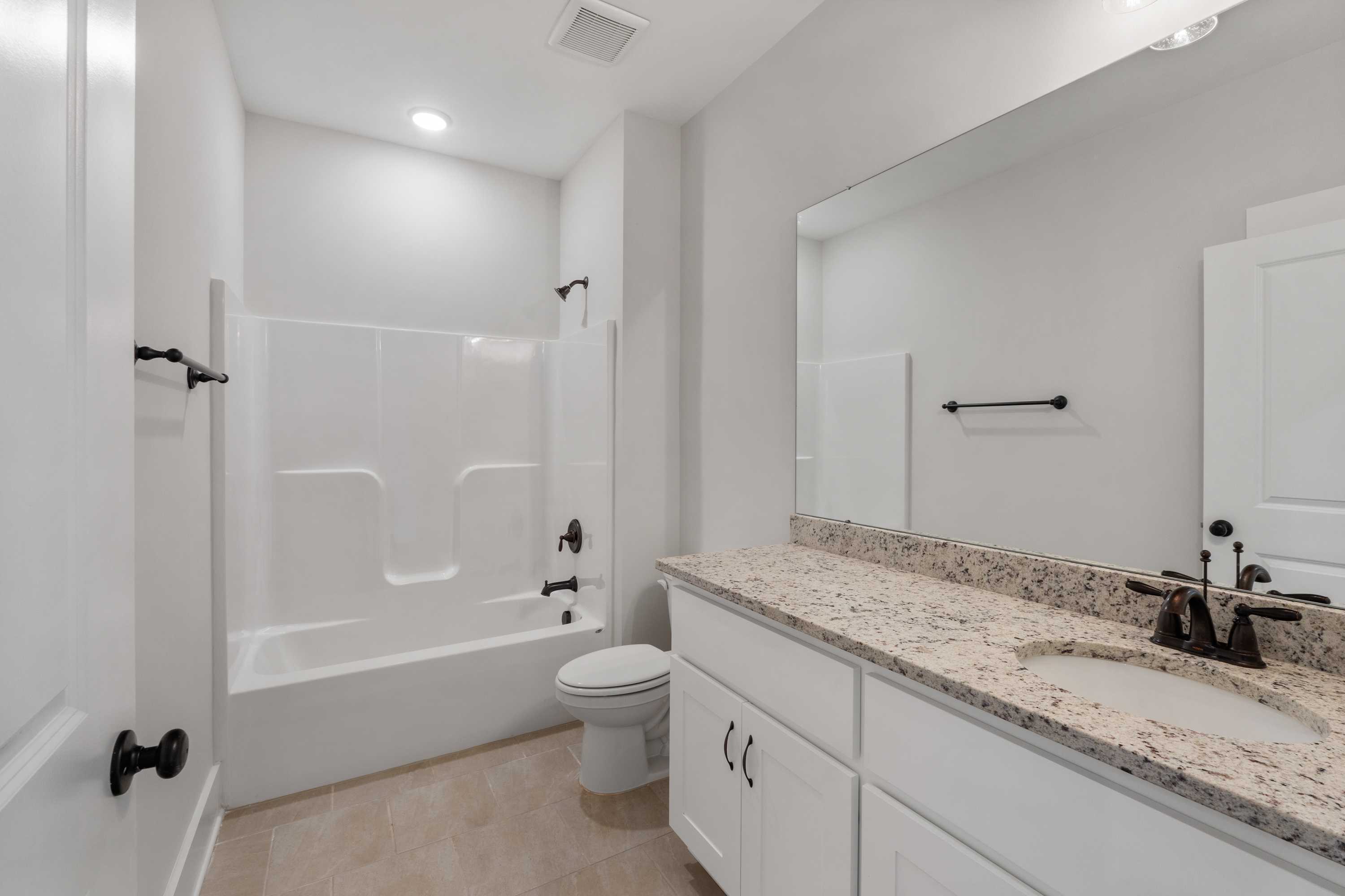 Spacious modern bathroom at The Villas at Barnett's Crossing in Madison Alabama with white tub-shower combo, granite vanity, large mirror