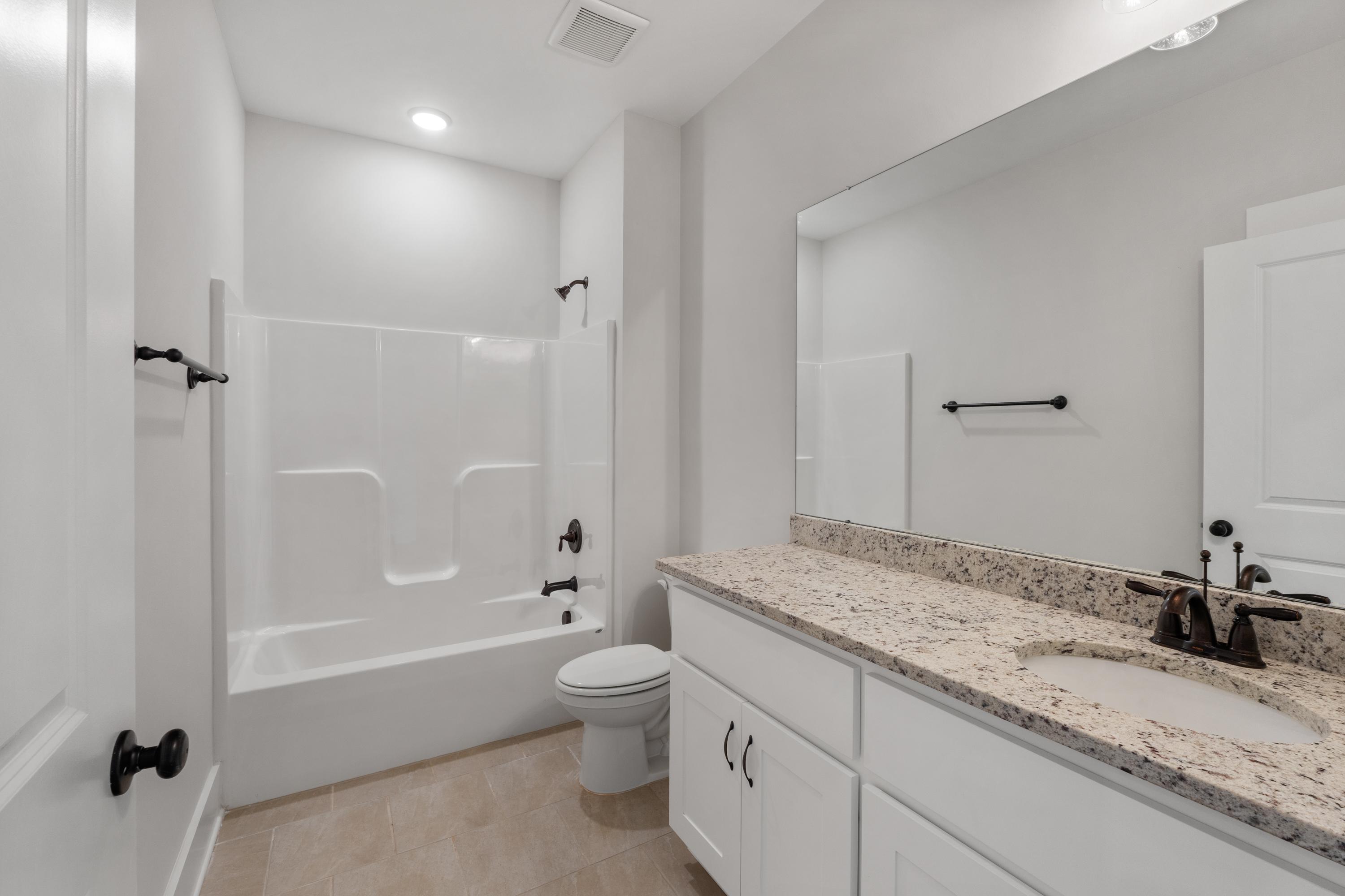 Spacious modern bathroom at The Villas at Barnett's Crossing in Madison Alabama with white tub-shower combo, granite vanity, large mirror