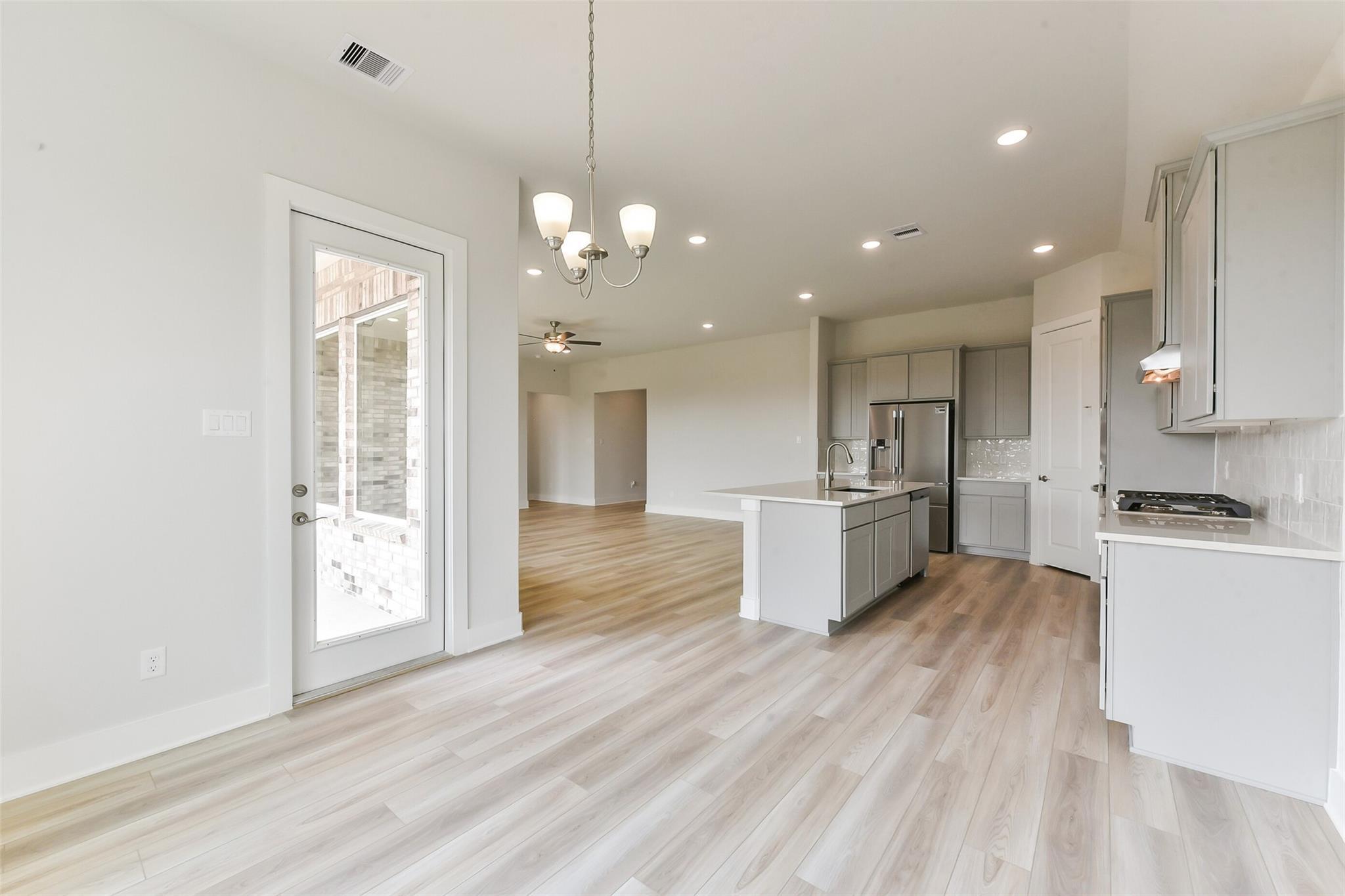 Open-concept kitchen with white shaker cabinets, stainless appliances, quartz island, and French doors to patio in Davidson Homes Edward A, Lago Mar