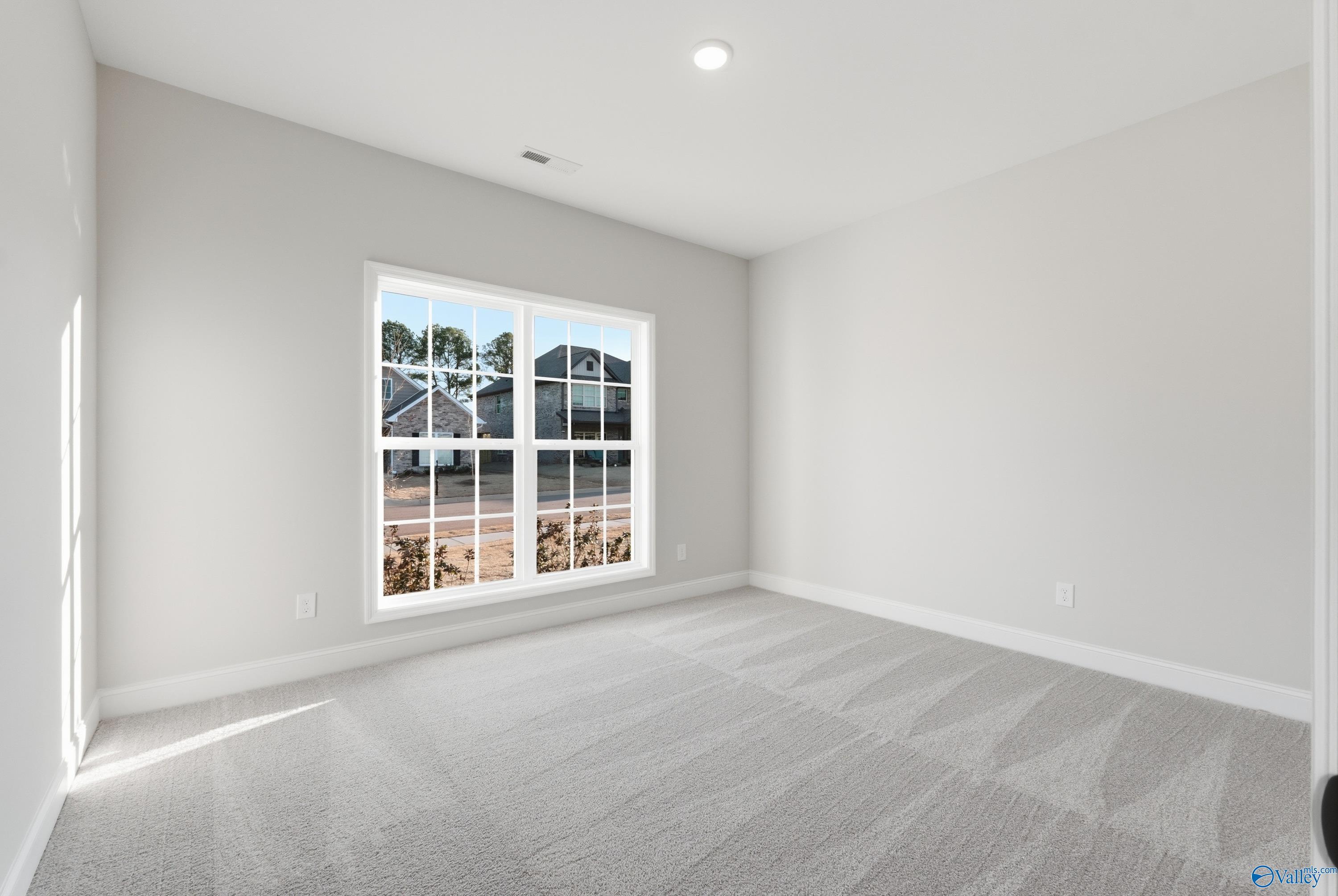 Sunlit empty bedroom with large window overlooking trees, gray carpet and walls in 4-bedroom Davidson Homes The Daphne C, Athens AL