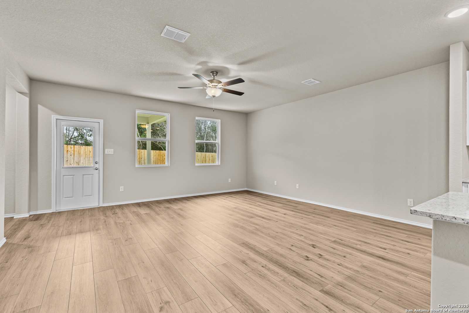 Bright open living room with light hardwood floors, ceiling fan, and large windows in Davidson Homes Douglas F, San Antonio